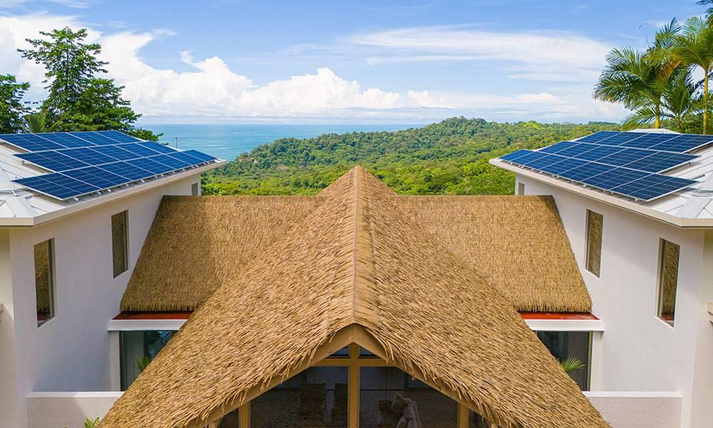 This property combines a distinct thatched roof with modern white roof sections and solar panels, enjoying abundant natural light and a sweeping view of the jungle and distant ocean.