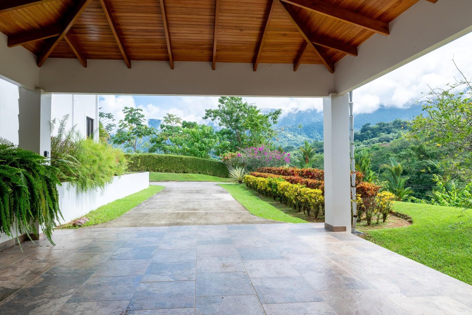 A covered entrance features a vaulted wooden ceiling, tiled floor, and open views of tropical landscaping and distant jungle-covered mountains.