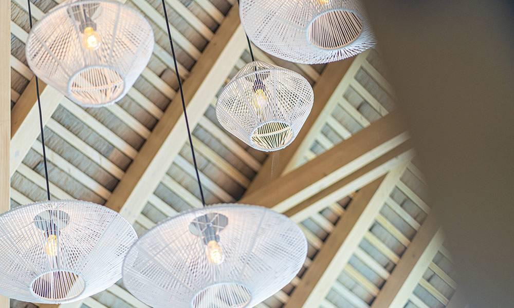 The high vaulted ceiling with exposed wooden beams is accented by several woven pendant lights, contributing to a spacious and organic feel.