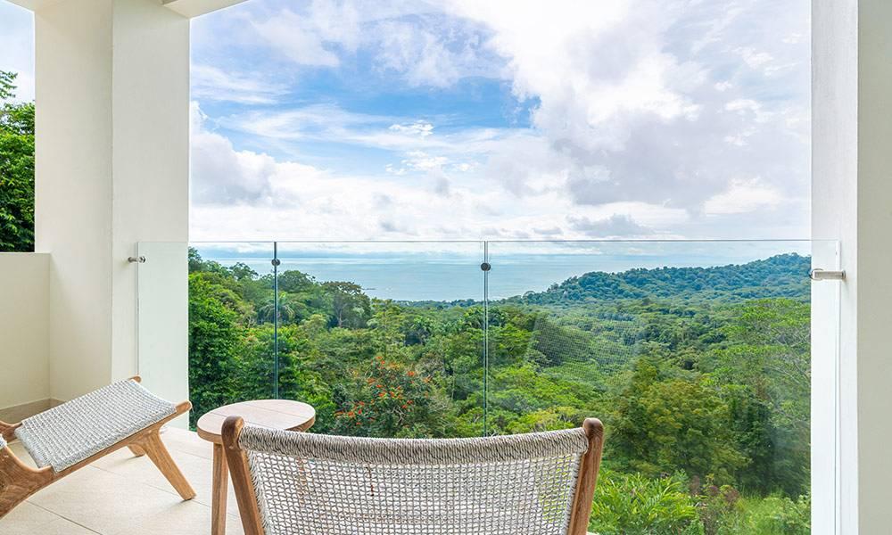This private balcony features a glass railing, providing abundant natural light and expansive views of the jungle and ocean beyond.