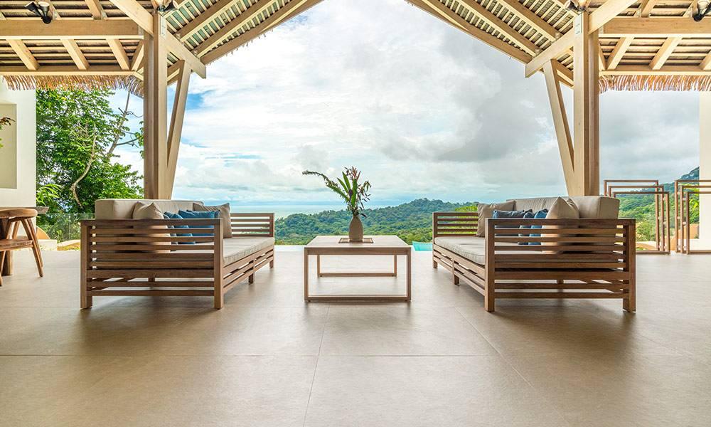 An expansive, open-air terrace with a high vaulted wooden ceiling provides comfortable lounge seating and unobstructed panoramic views of the jungle and distant ocean.