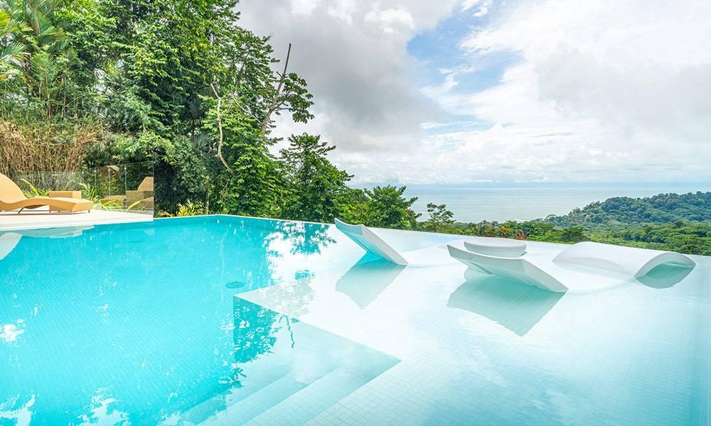 This infinity pool, featuring in-water loungers and a poolside terrace, offers an expansive, bright space with panoramic views of the ocean and lush jungle.