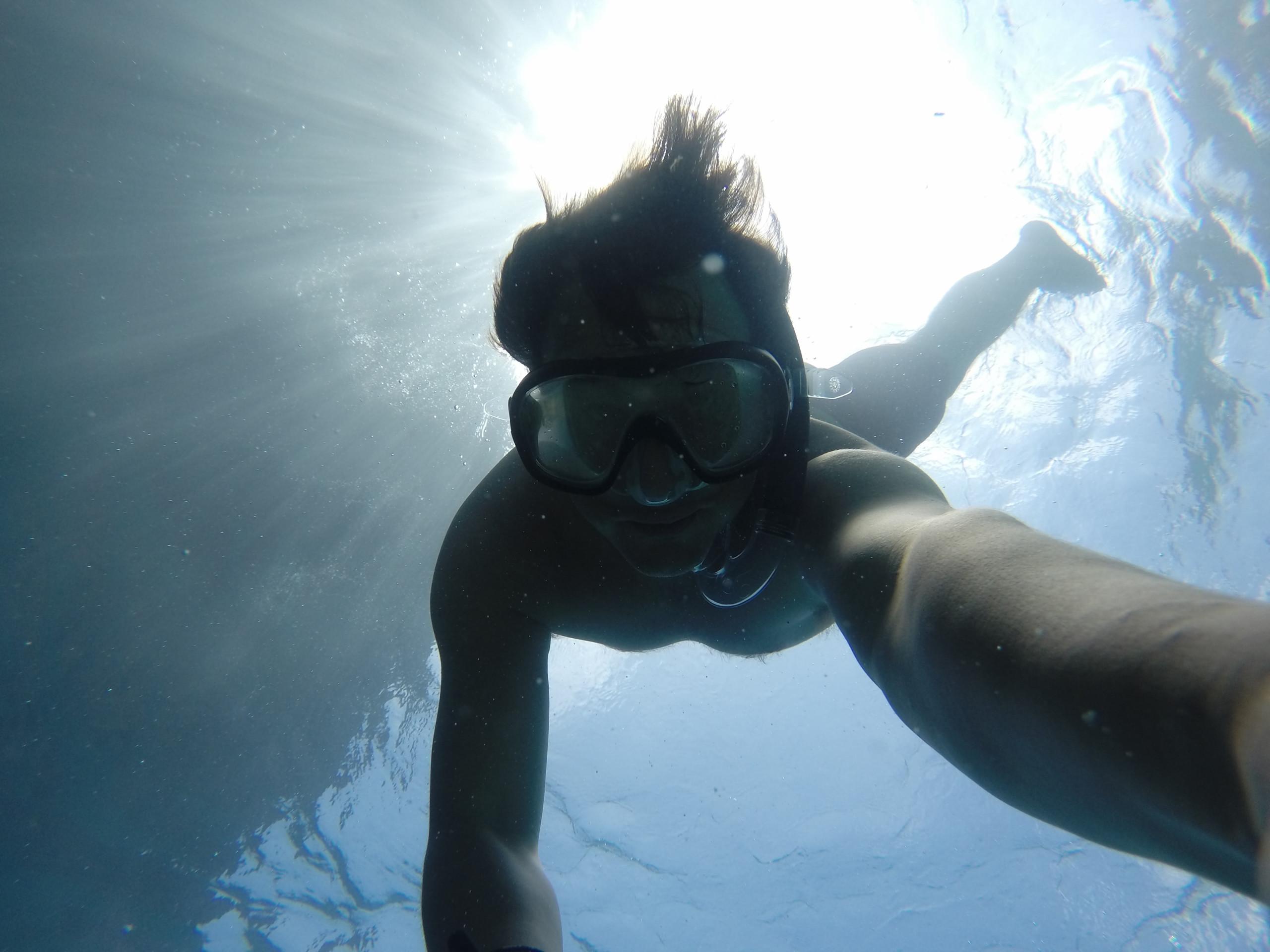 Natural light filters through the water's surface, revealing a person wearing a snorkel mask underwater.