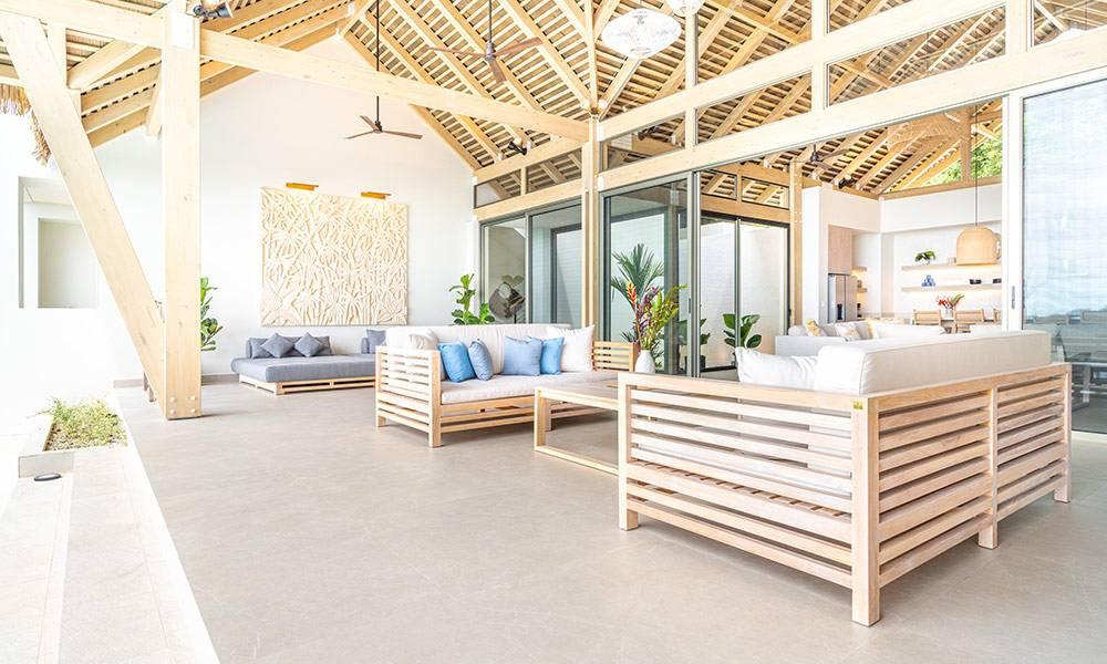 An open-plan living area with high vaulted wooden ceilings and exposed beams provides ample natural light and multiple seating areas, connecting to adjacent spaces through large glass doors.