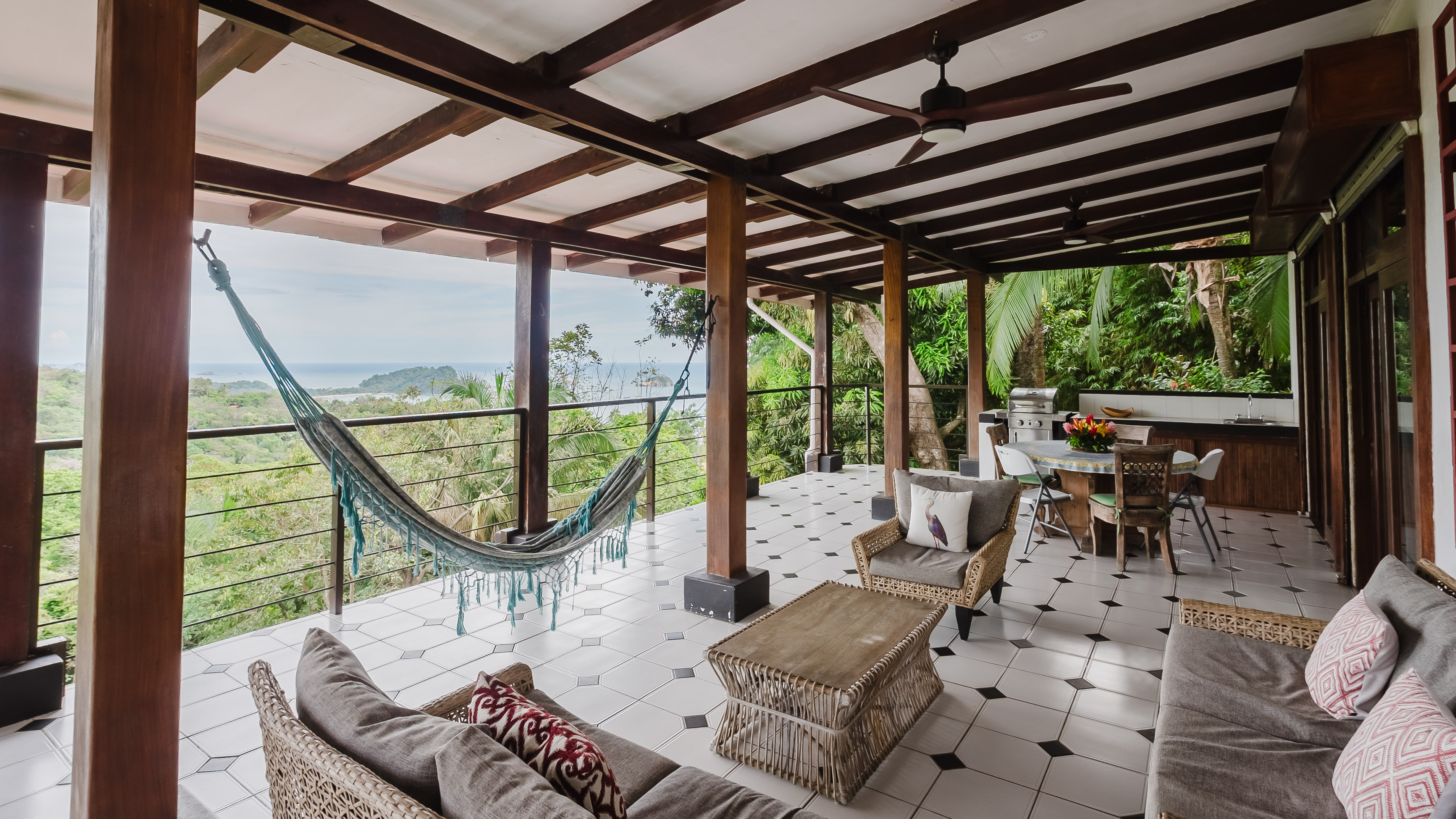 An open-air covered terrace offers a spacious lounge and dining area with an outdoor kitchen, featuring a hammock and expansive views of the ocean and surrounding tropical forest.