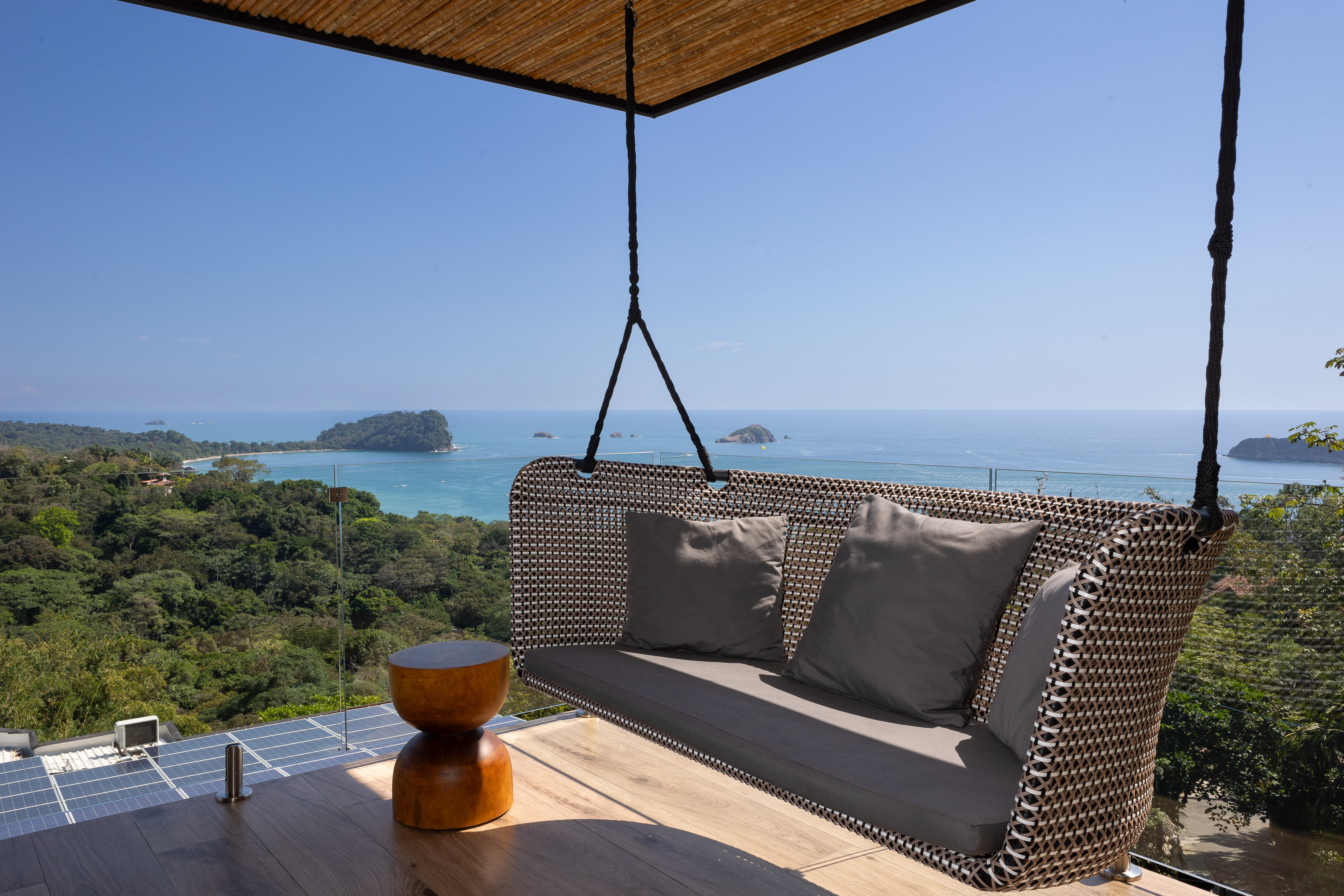 An open-air terrace with a suspended sofa provides unobstructed ocean and jungle views under bright natural light.