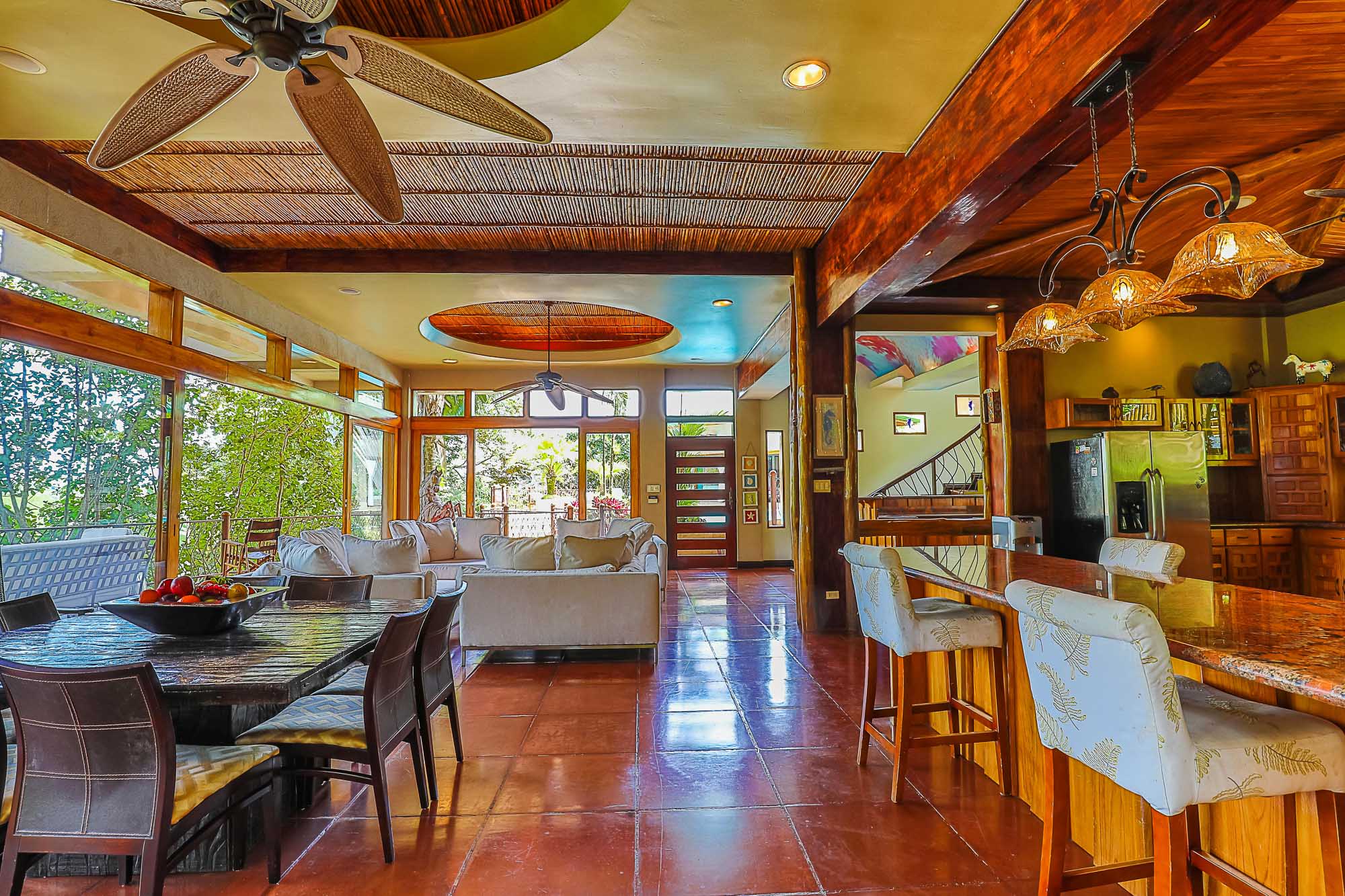 This bright open-plan space, integrating living, dining, and kitchen areas, features natural wood accents and large windows that offer tropical rainforest views and abundant daylight.