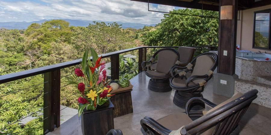 A covered terrace with a built-in jacuzzi and lounge seating overlooks a verdant jungle canopy and distant mountains.