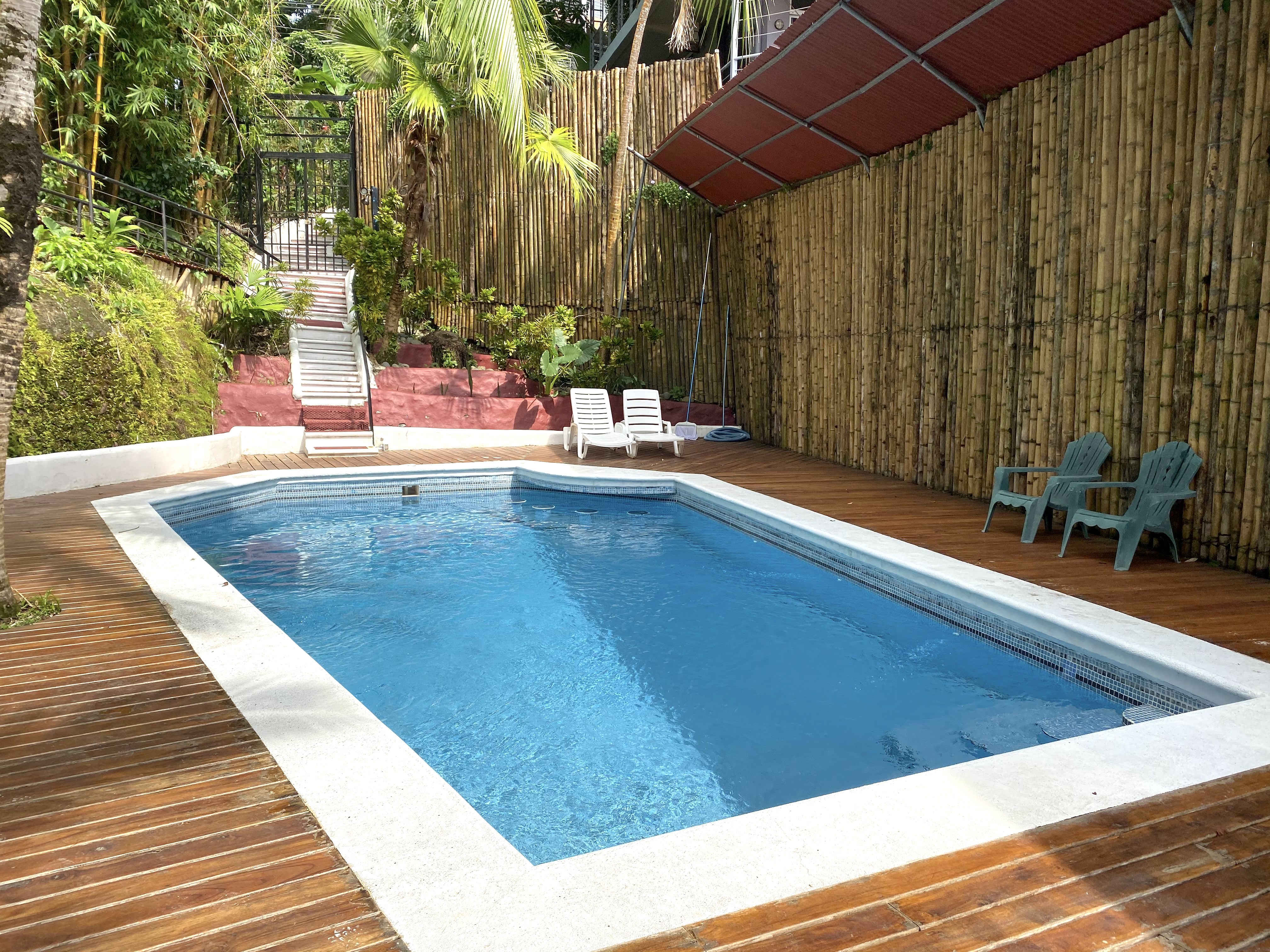The outdoor swimming pool area features a wooden deck, a tall bamboo fence, and abundant tropical foliage providing natural privacy.