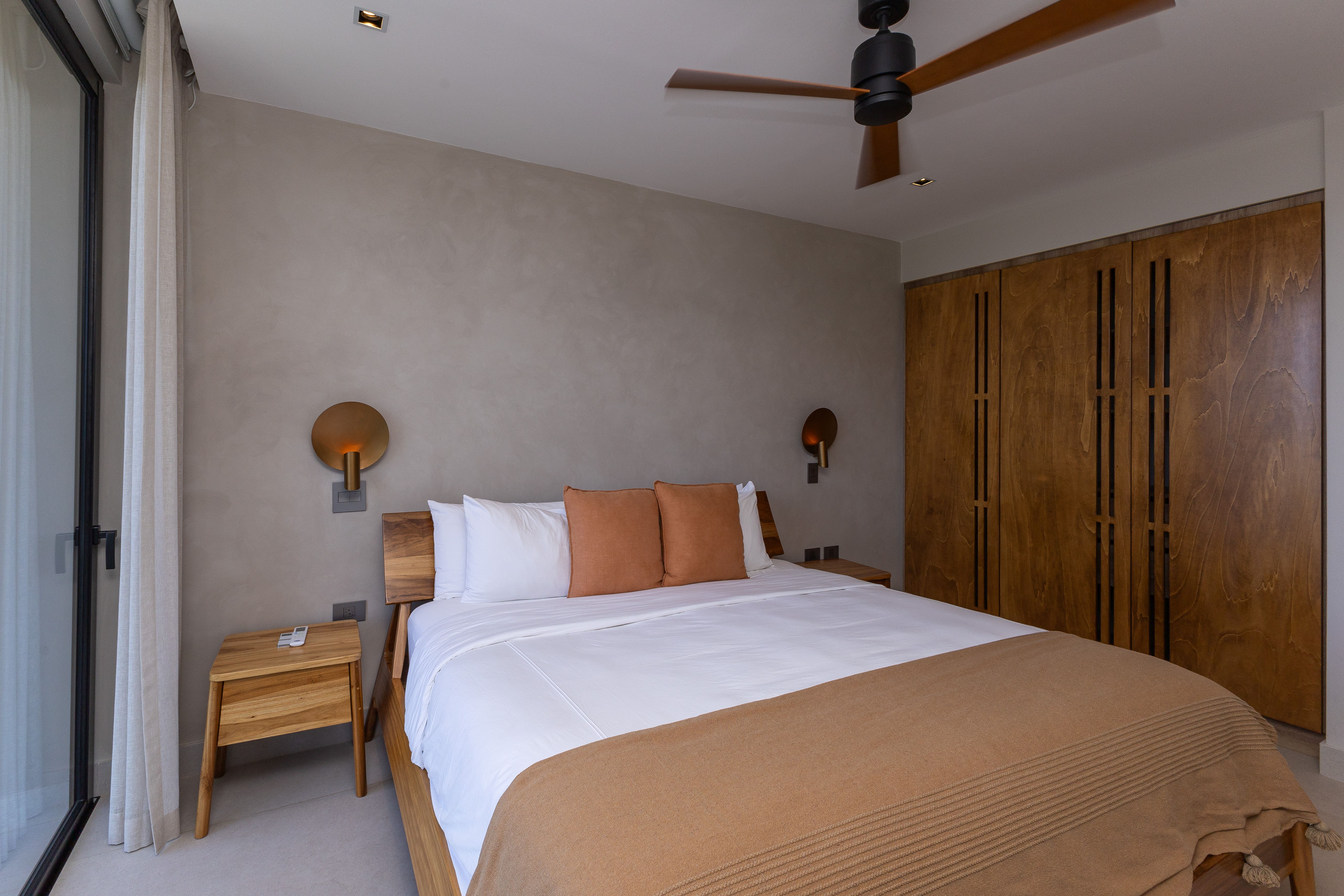 This contemporary bedroom features a king-size bed, warm wooden details, and a large glass door inviting natural light and scenic views.