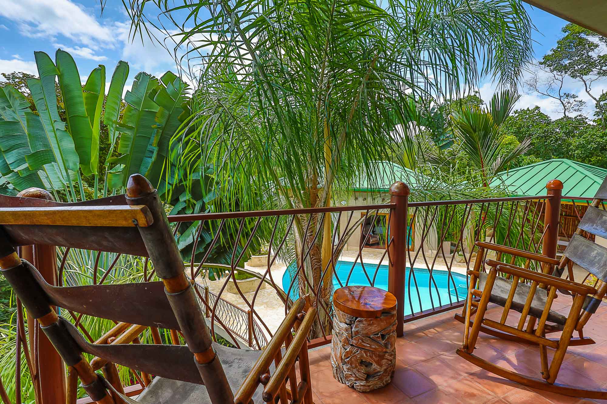 An open-air terrace with a tiled floor and rustic wooden seating overlooks the inviting pool and surrounding tropical forest under natural light.