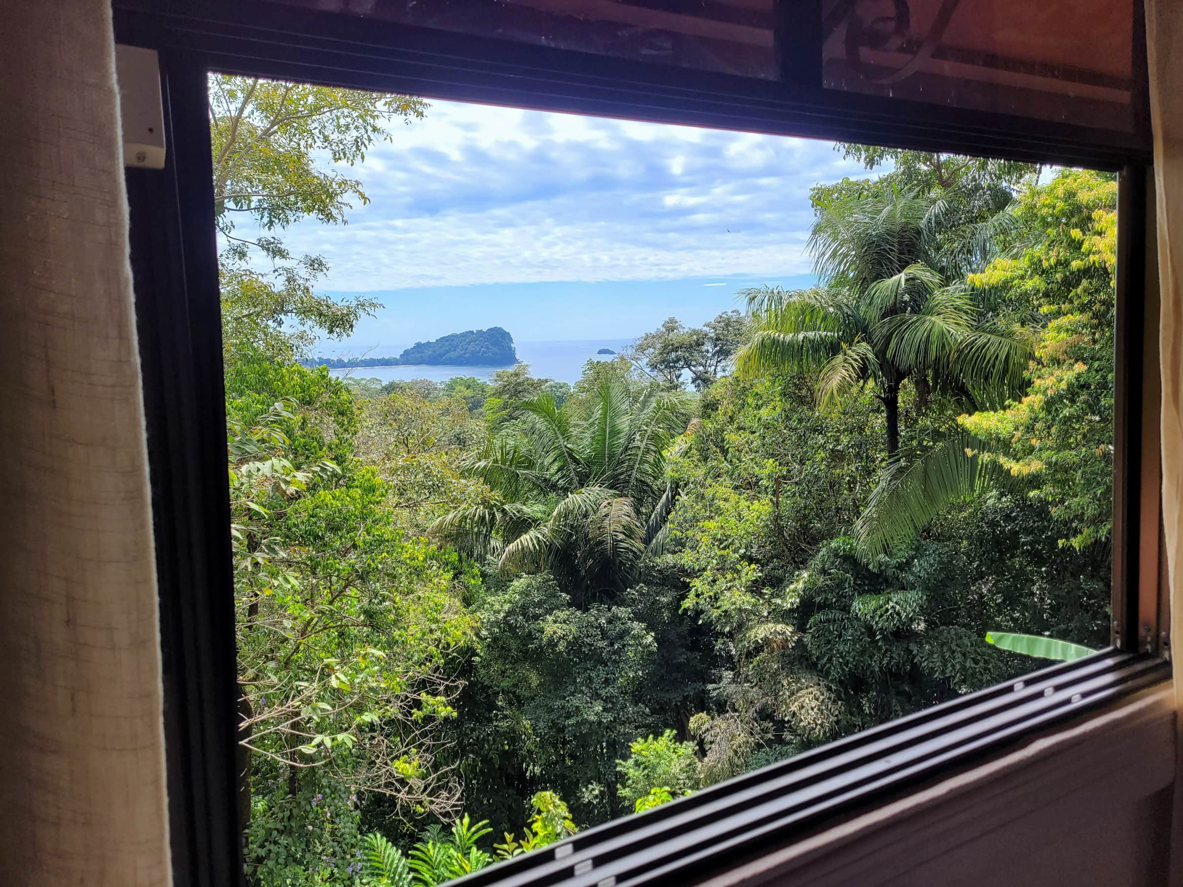 A large window provides an immersive view of the tropical jungle canopy and the Pacific Ocean with a distant island.