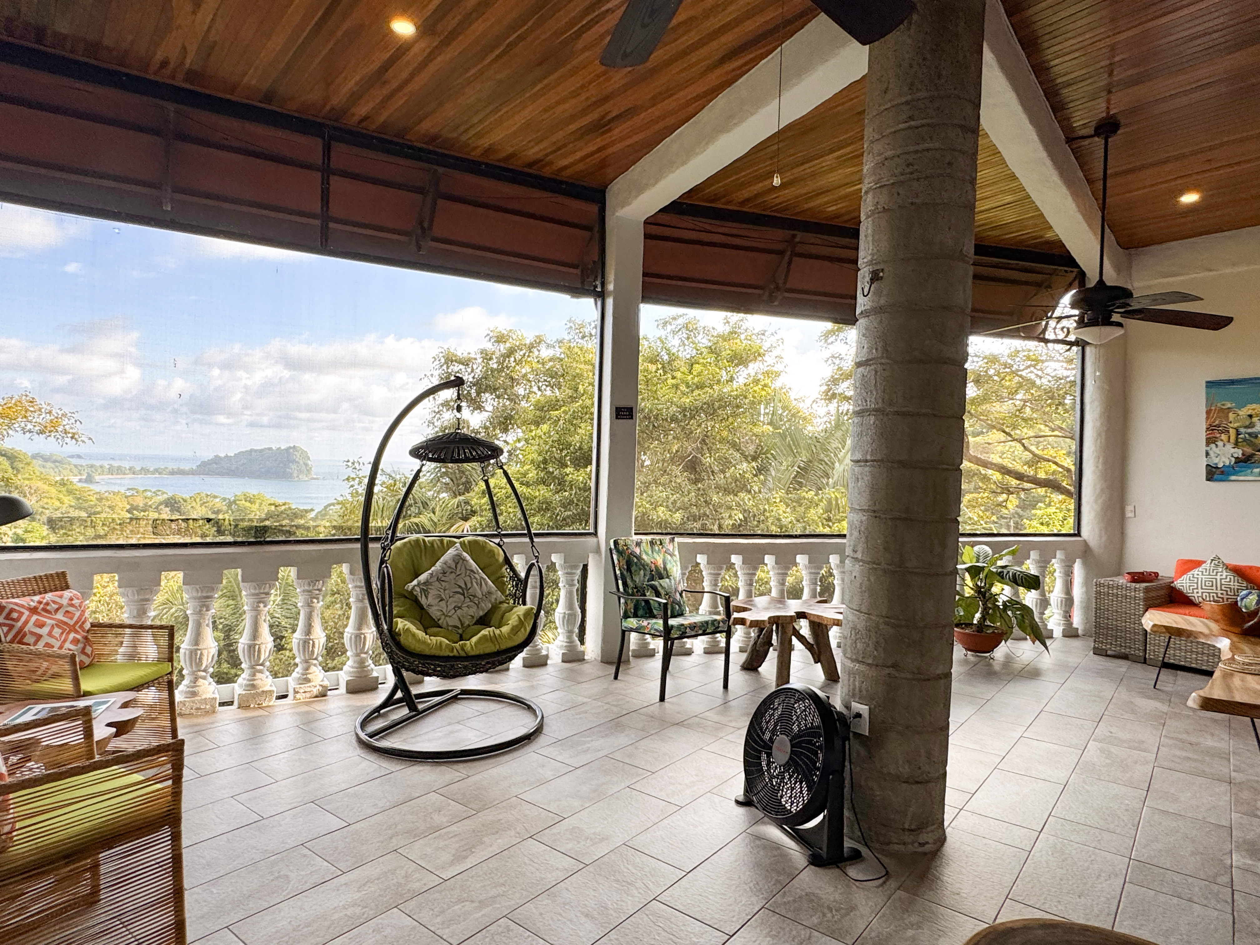An open-air terrace with a wood-slatted ceiling and tiled floor looks out over the ocean and tropical jungle.
