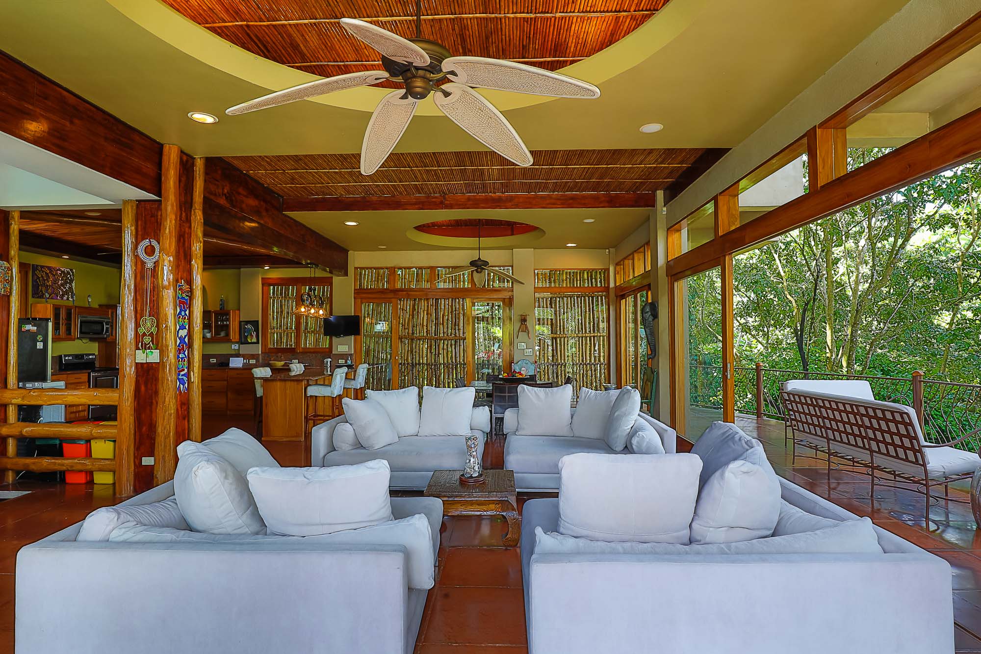 The open living room combines comfortable seating with natural wood and bamboo architectural elements, offering abundant light and direct views into the surrounding rainforest.