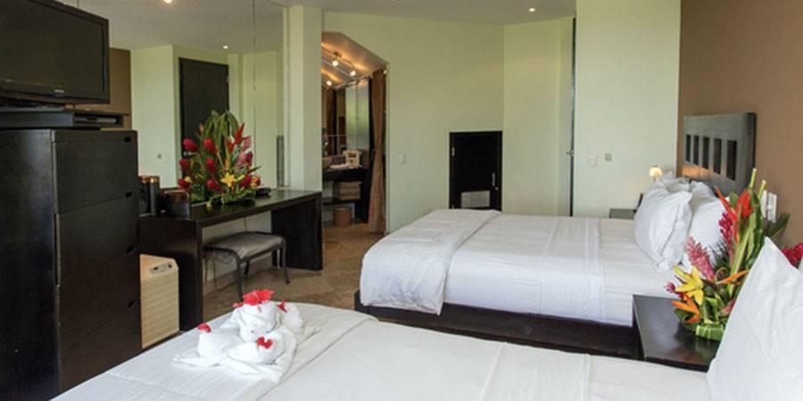 This well-lit bedroom features two queen beds and an open archway leading to a private bathroom, providing a comfortable and private guest space.