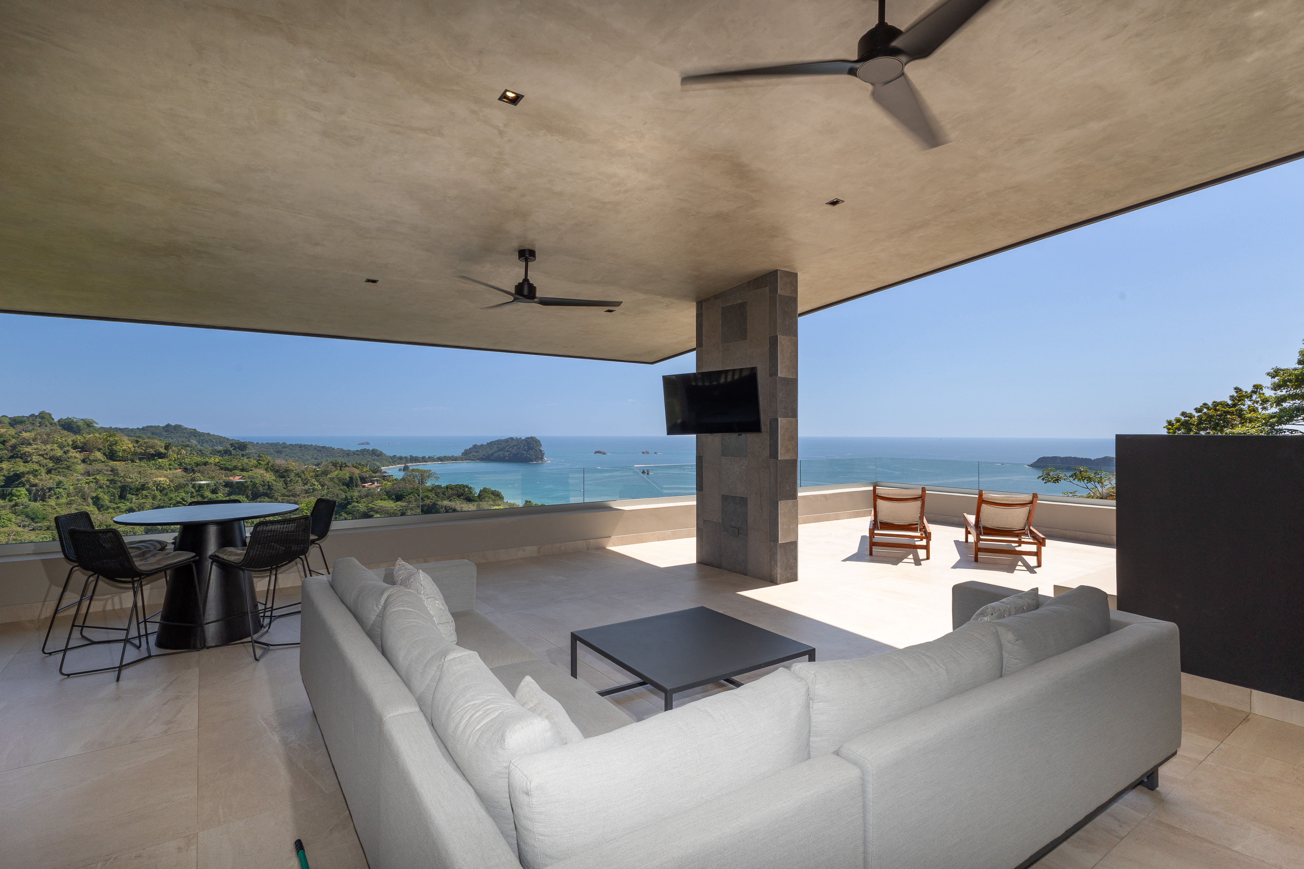 An expansive, shaded terrace features comfortable outdoor seating and dining areas, offering panoramic views of the Pacific coastline and lush jungle.