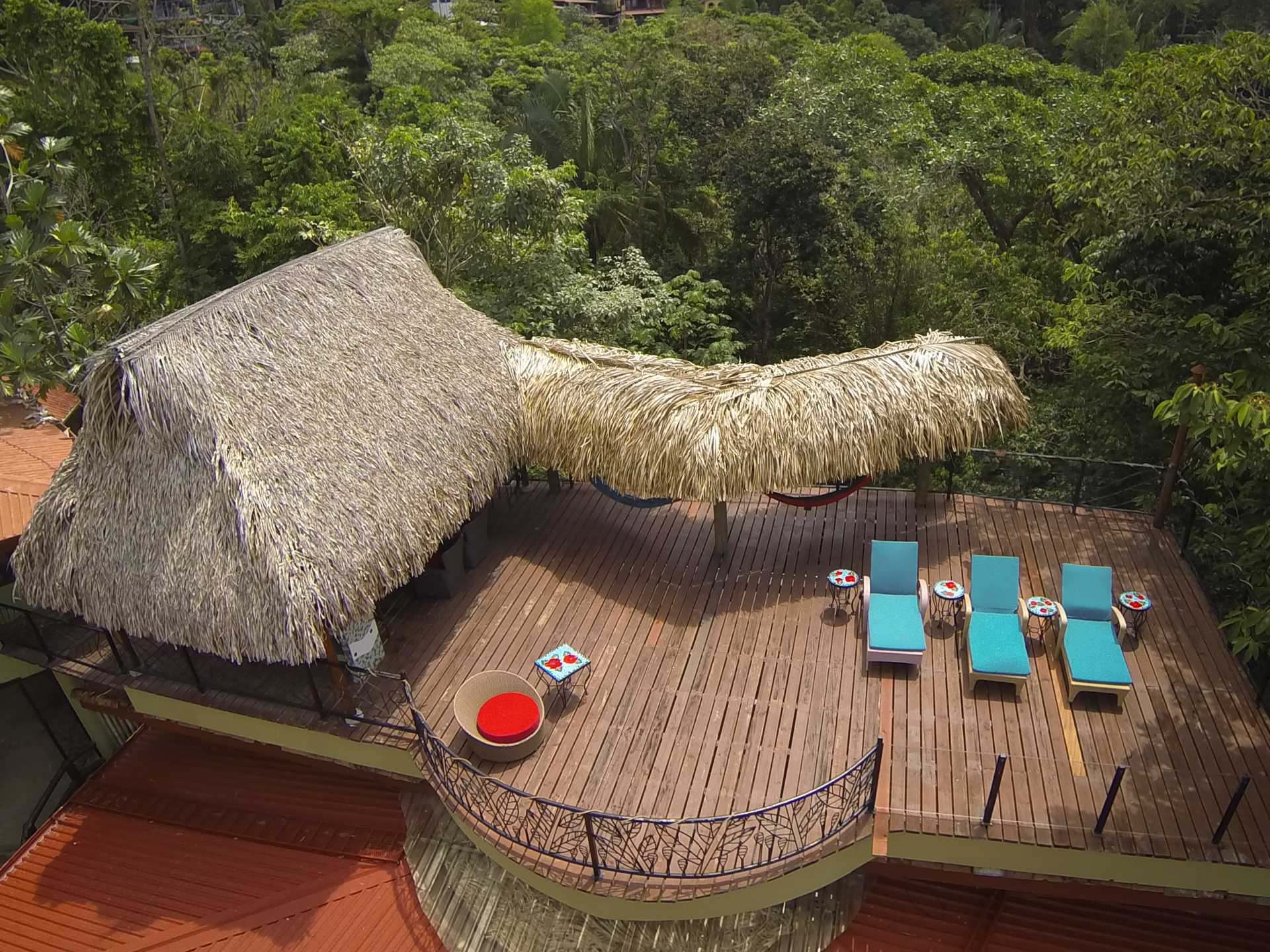 An elevated wooden deck, partially shaded by a thatched roof, offers lounge seating with views extending into the jungle canopy.
