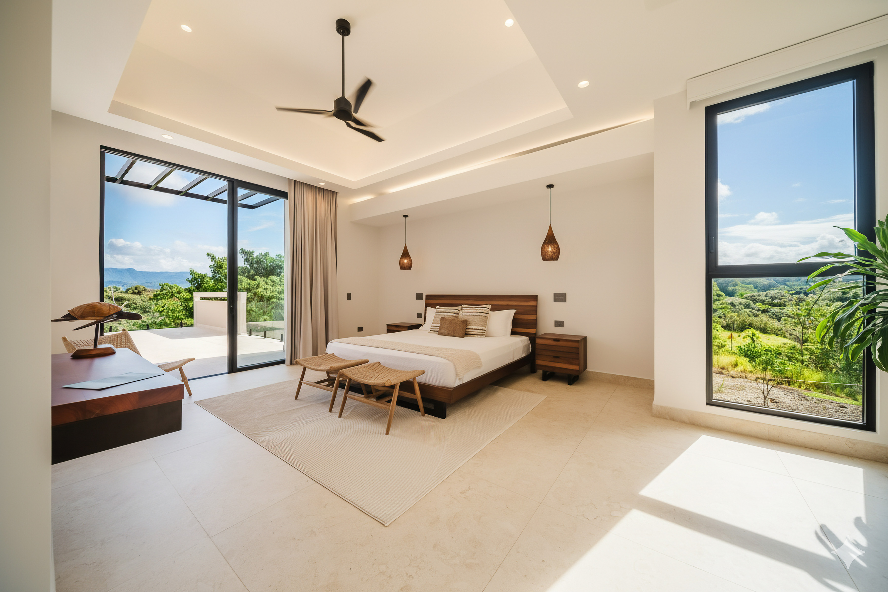 This bright bedroom features a king-size bed, a tray ceiling, and natural light from large sliding doors leading to a terrace and a window with views of tropical hills.