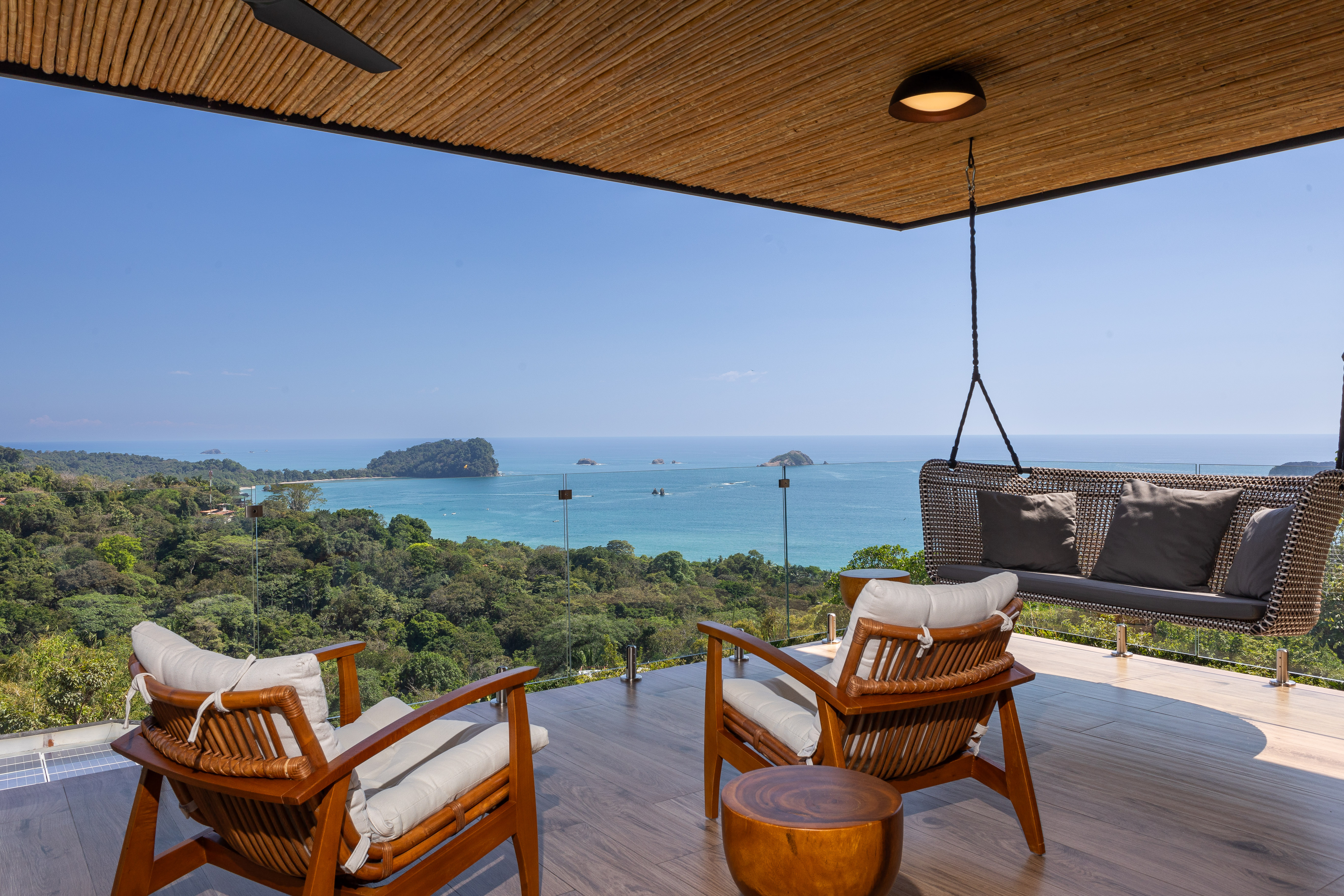 An outdoor terrace provides lounge seating under a bamboo ceiling, framing expansive views of the Pacific Ocean and verdant jungle.
