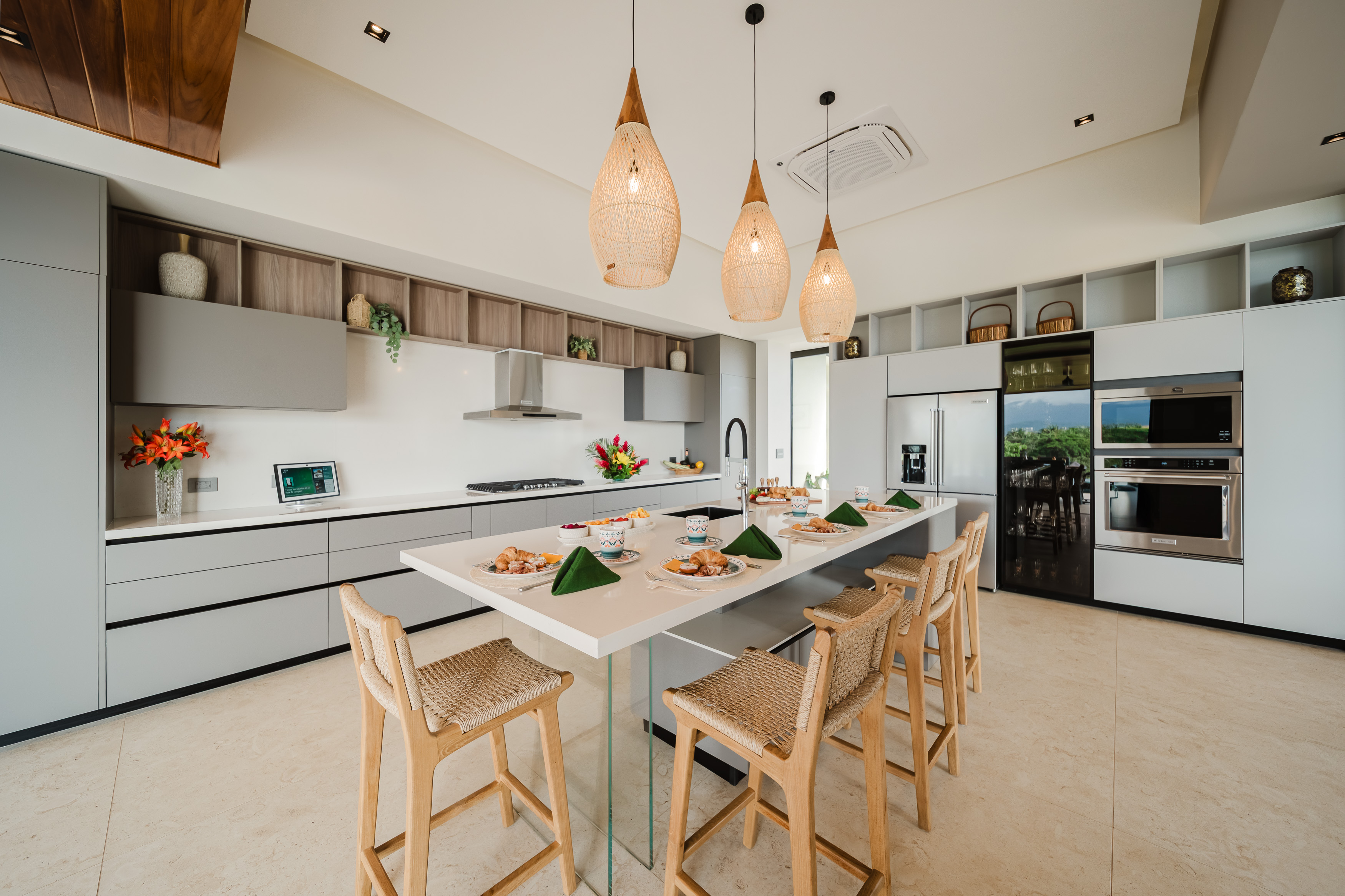 A bright, contemporary kitchen features light grey cabinetry, a large island with bar seating, integrated appliances, and views to the outdoors.