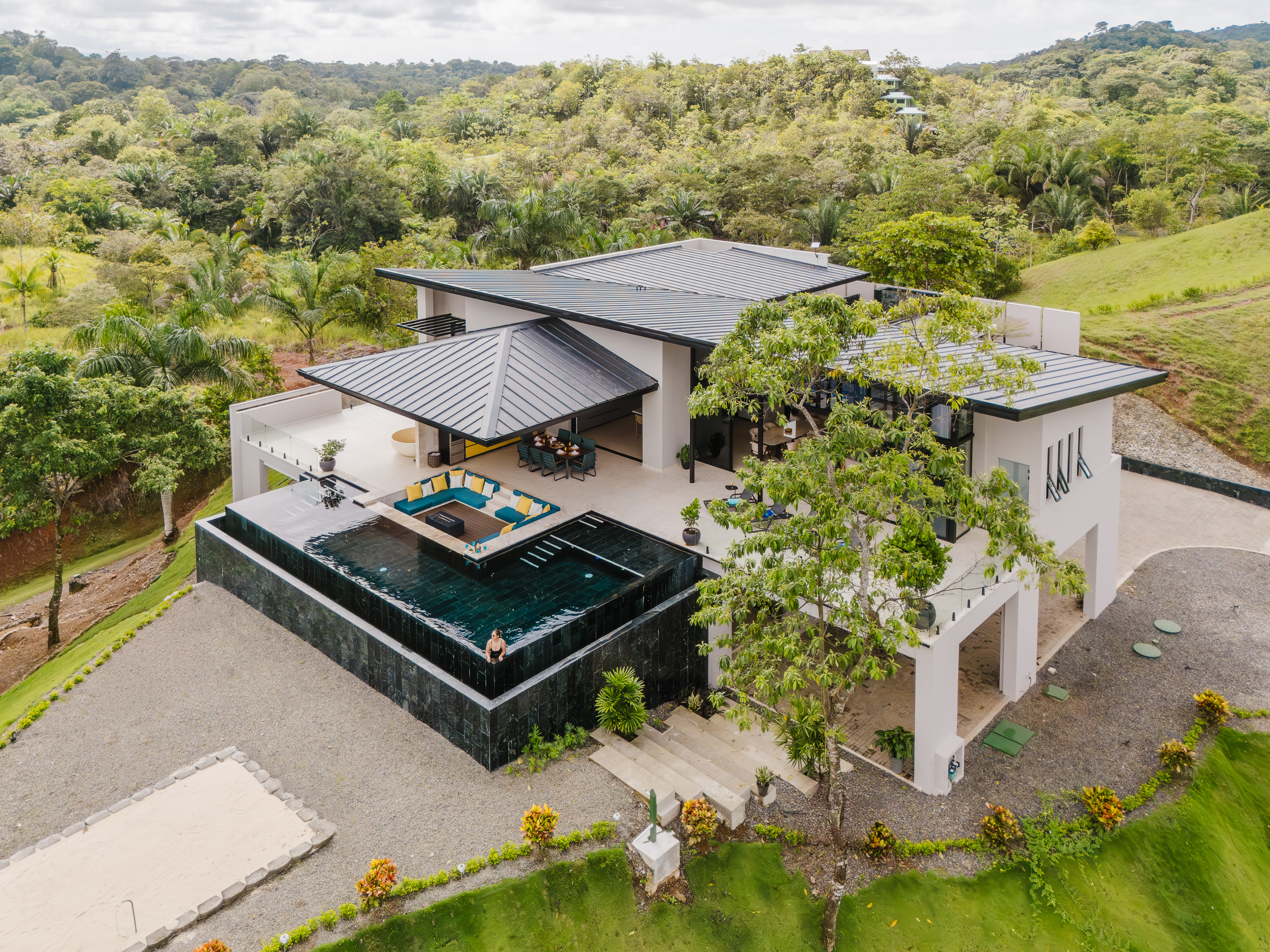 A contemporary villa with tiered swimming pools and open-air lounging spaces, integrated into a vibrant tropical forest setting.