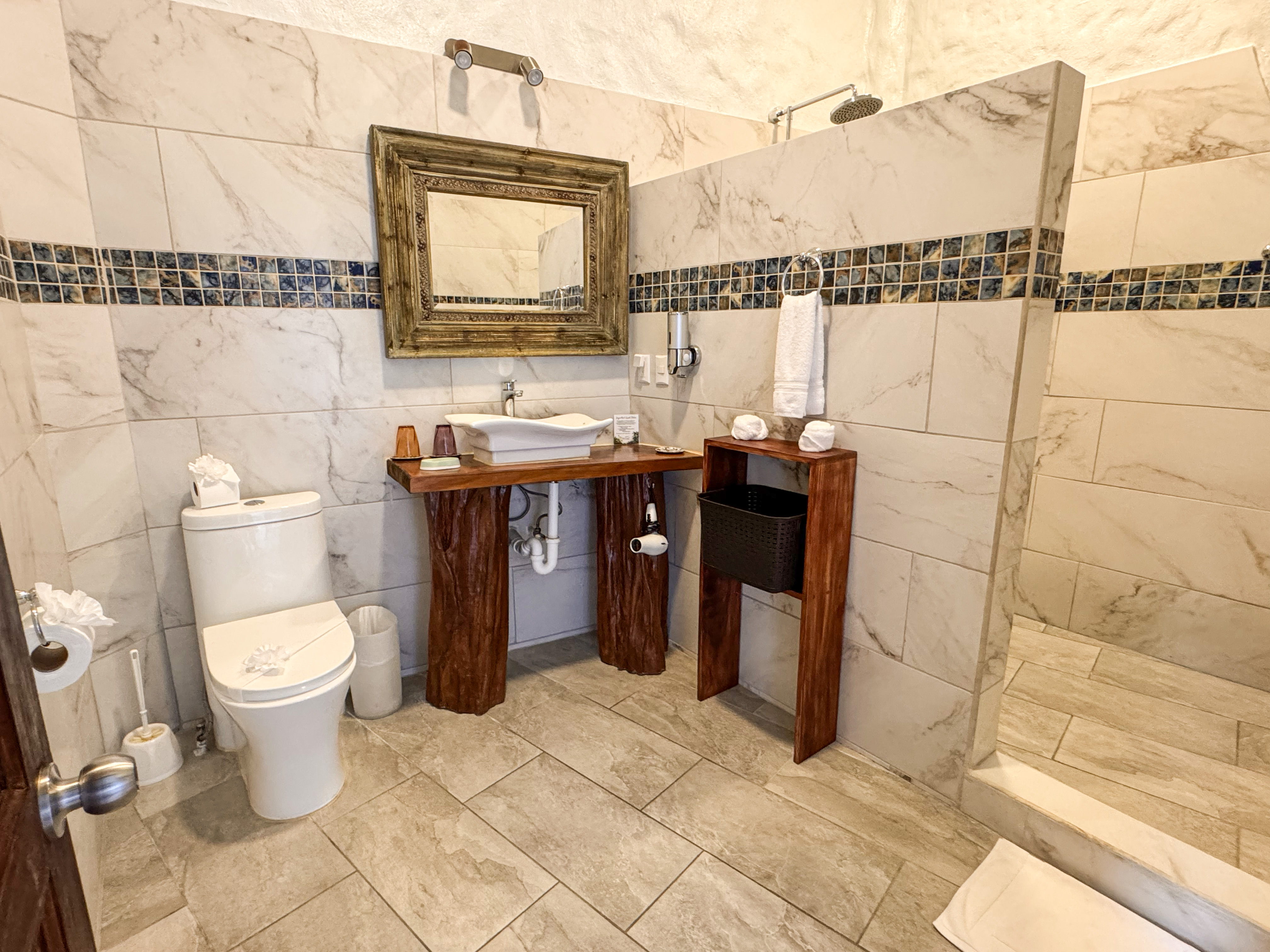 The bathroom features white marble-look tiled walls with a decorative mosaic band, a rustic wood vanity with a vessel sink and framed mirror, and a walk-in shower.