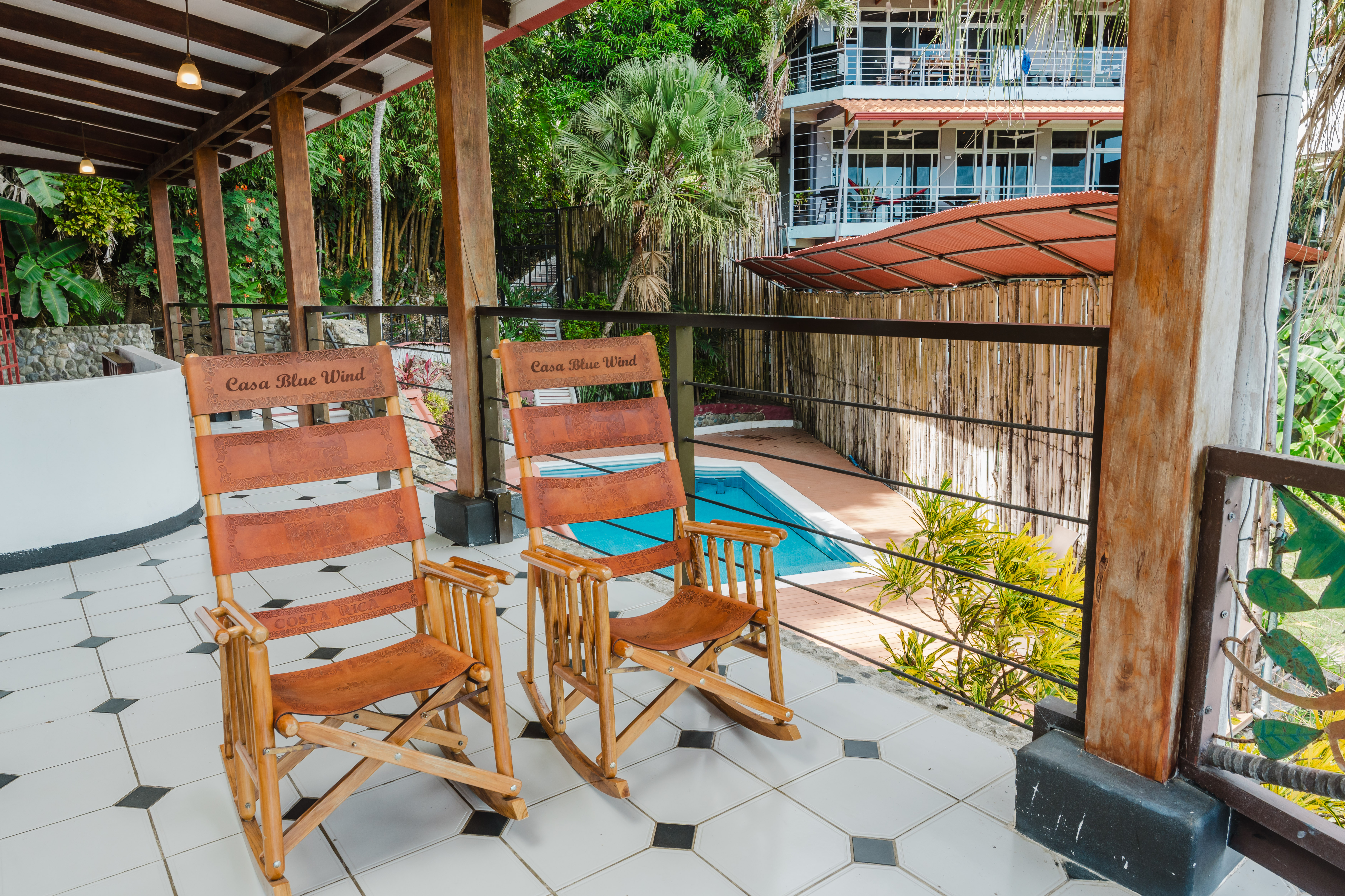 A covered terrace with a tiled floor and wooden support beams offers a comfortable seating area with views of the private pool and lush tropical gardens.