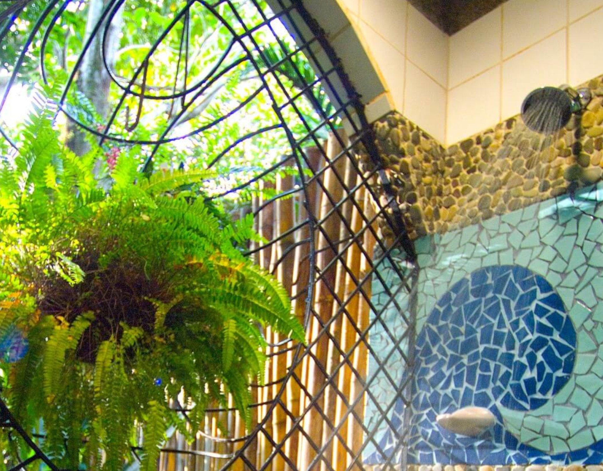 The shower combines river stone and mosaic tiles with an open archway offering views of vibrant jungle greenery.