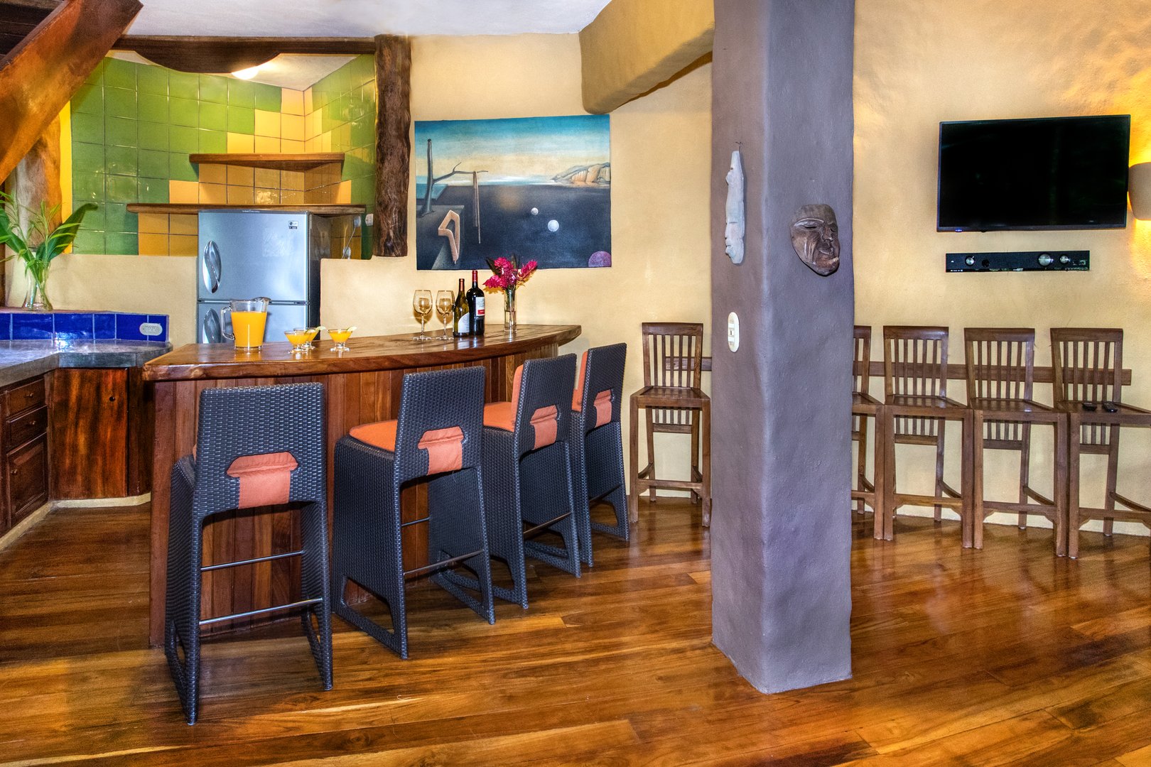 A warm lounge area features a polished wooden wet bar with seating, a functional refrigerator, and a tiled backsplash, all set against rich wood flooring.