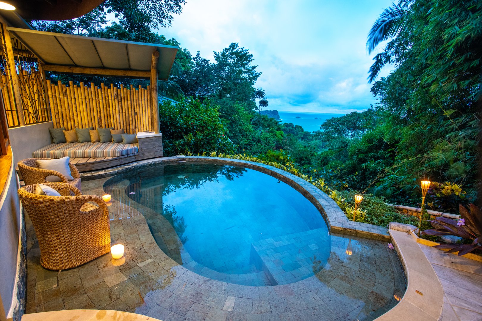 This secluded plunge pool area features a covered lounge with bamboo walls, offering expansive views of the ocean and surrounding jungle.