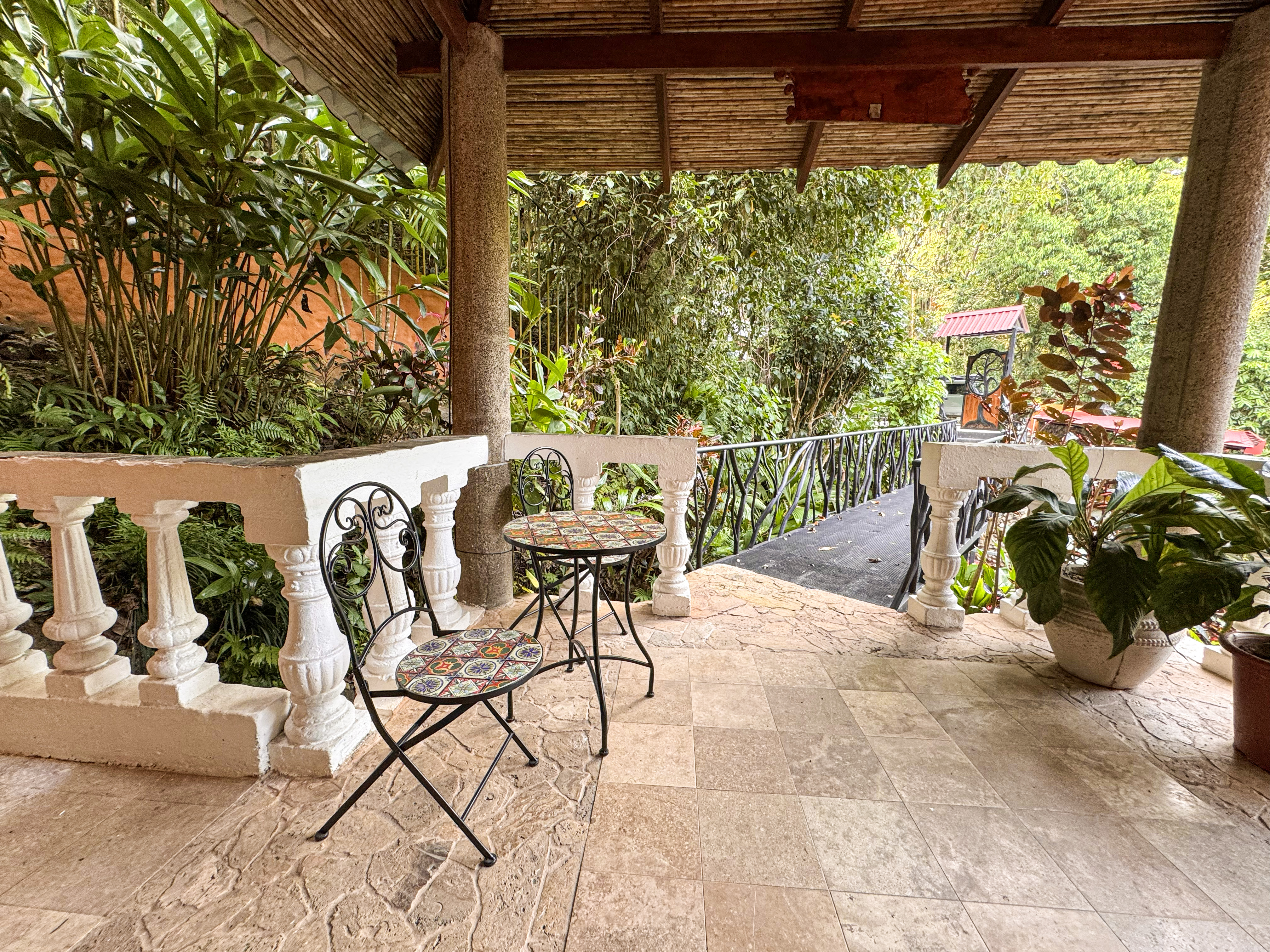 A covered terrace with a tiled floor and balustrade provides a shaded seating area immersed in dense tropical jungle views.