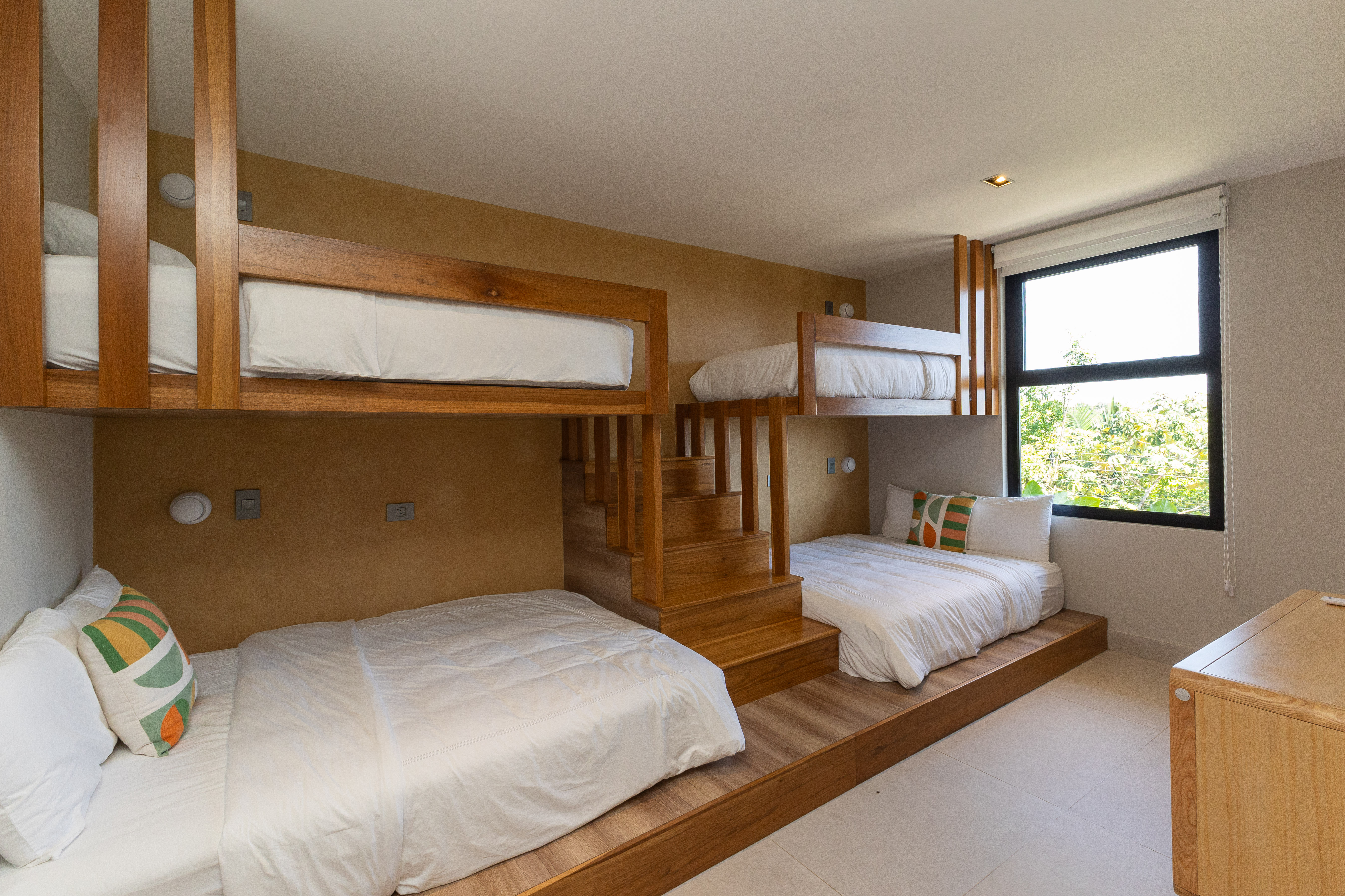 This bedroom features an integrated wooden bunk bed system for multiple guests, illuminated by natural light from a window framing lush jungle views.