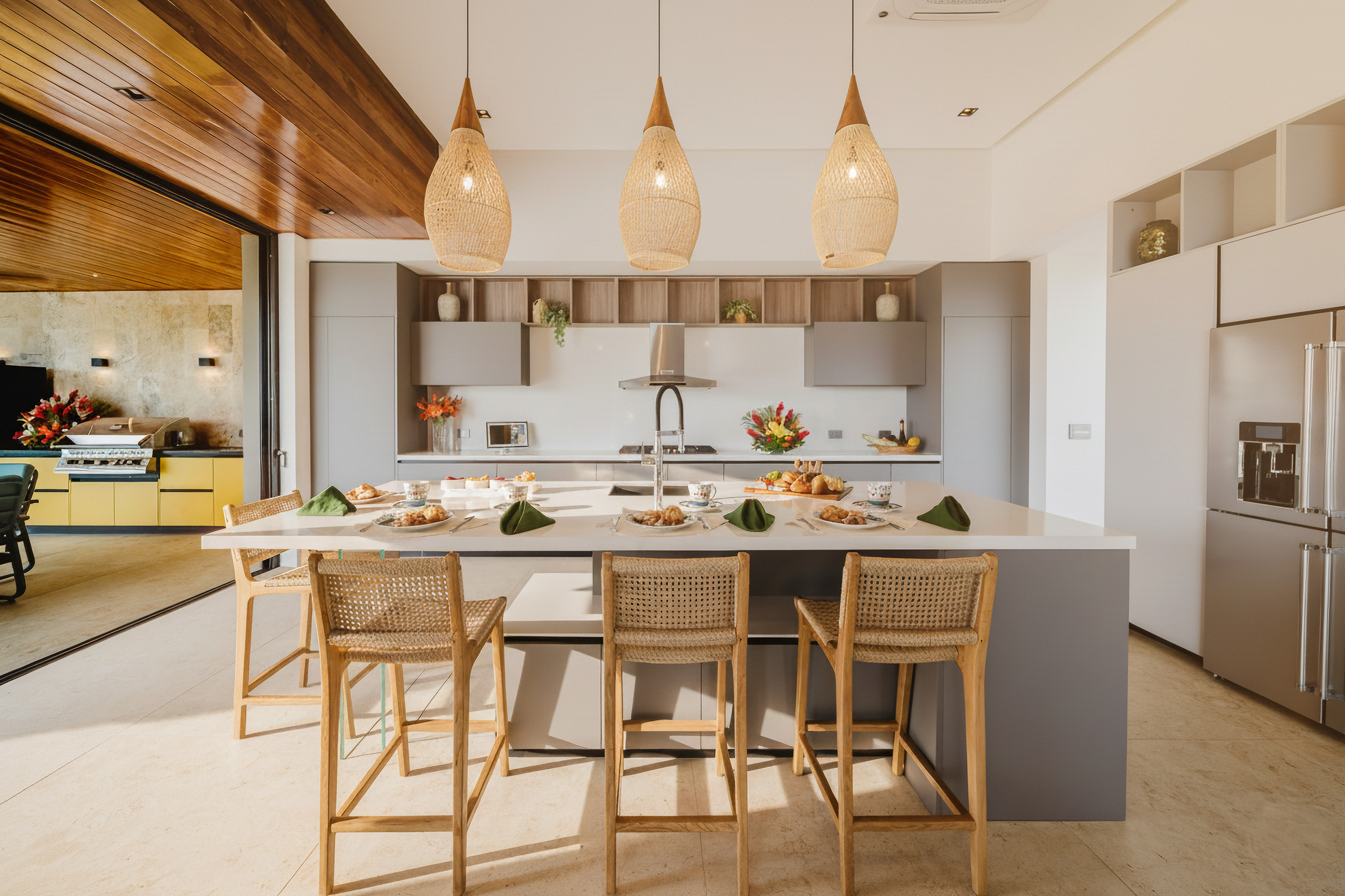 This bright kitchen features a large island with seating, modern appliances, and wide retractable doors opening to an outdoor grilling station.