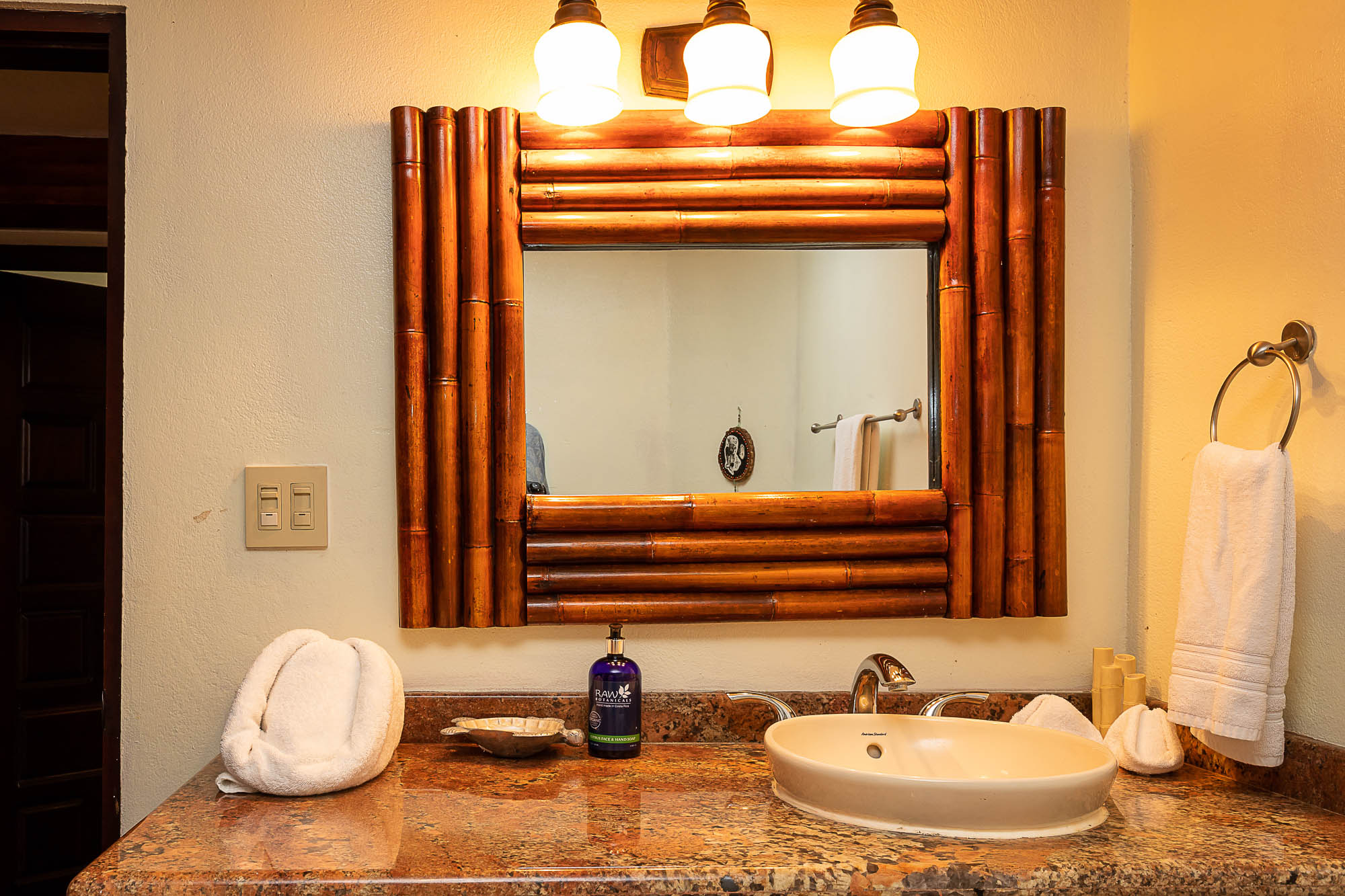 This bathroom features a vessel sink set in a speckled stone countertop, beneath a mirror framed with natural bamboo and illuminated by warm wall sconces.
