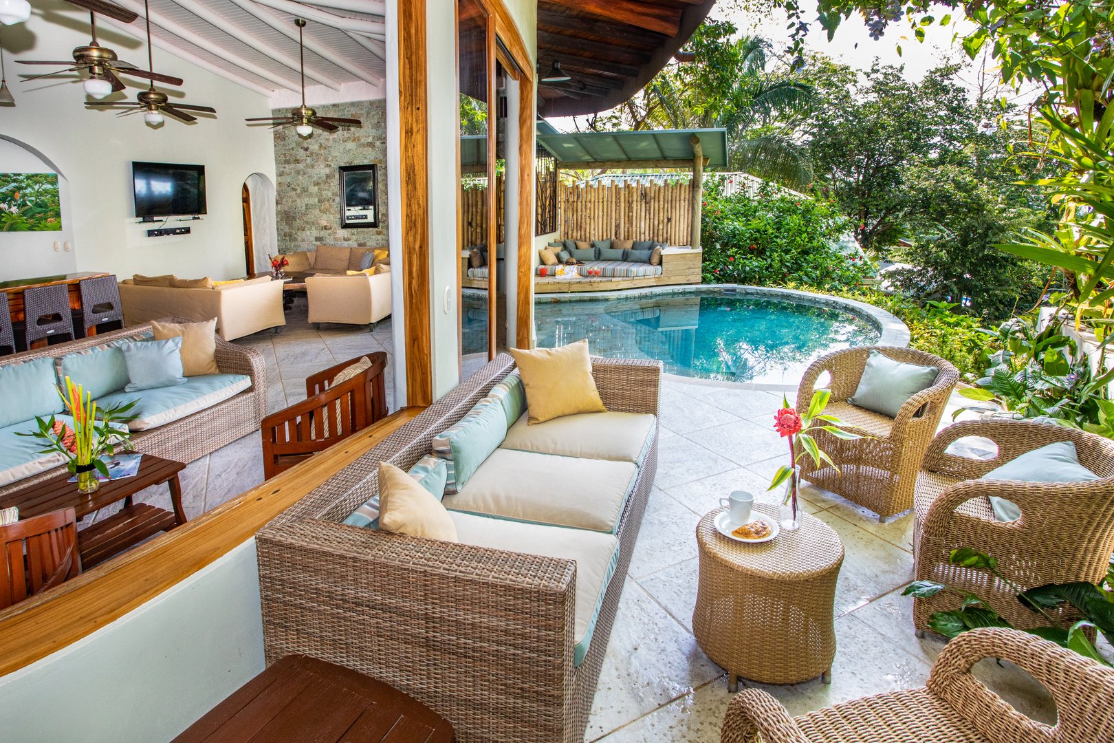 A spacious outdoor terrace with wicker seating and a circular tropical pool integrates seamlessly with an indoor living area featuring high ceilings and lush jungle views.