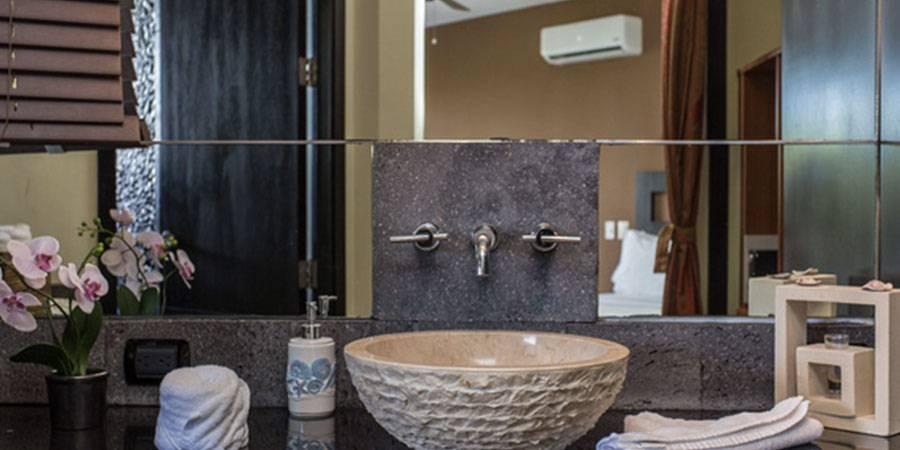 The private bathroom features a textured stone vessel sink and wall-mounted faucet, reflecting the comfortable adjacent bedroom.