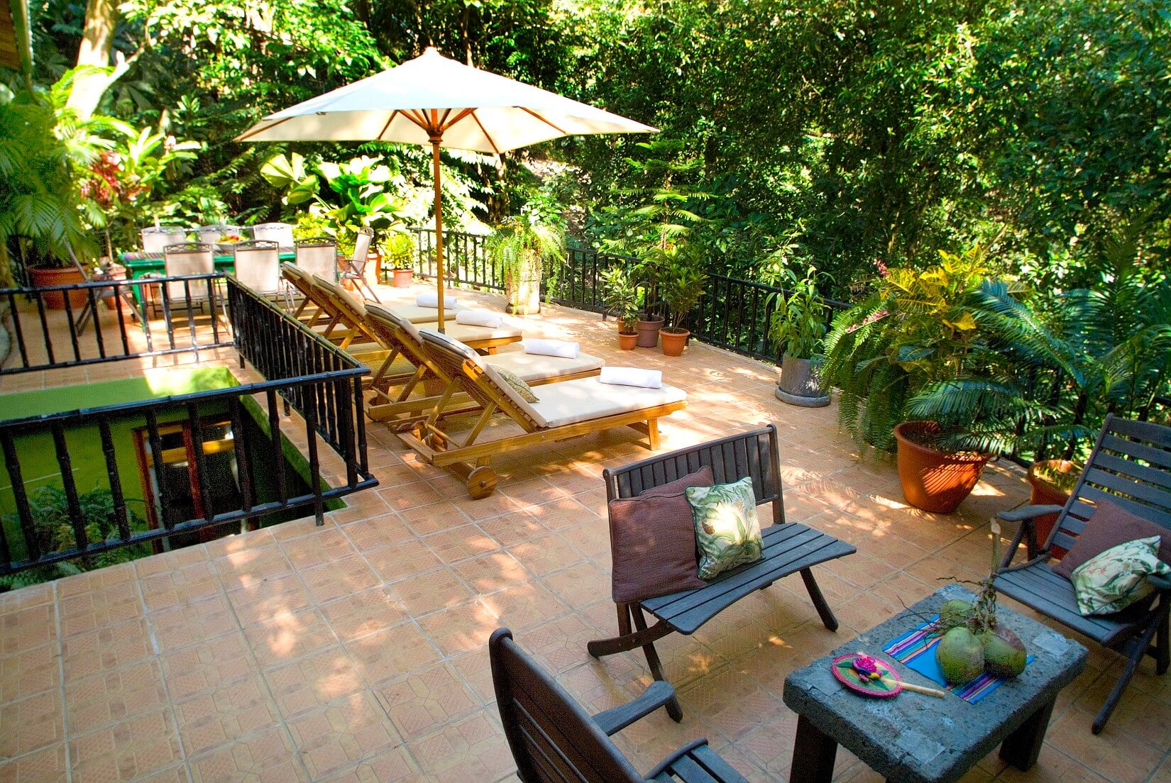 A multi-level outdoor terrace offers shaded lounge seating and a dining area, immersed in bright tropical jungle views.