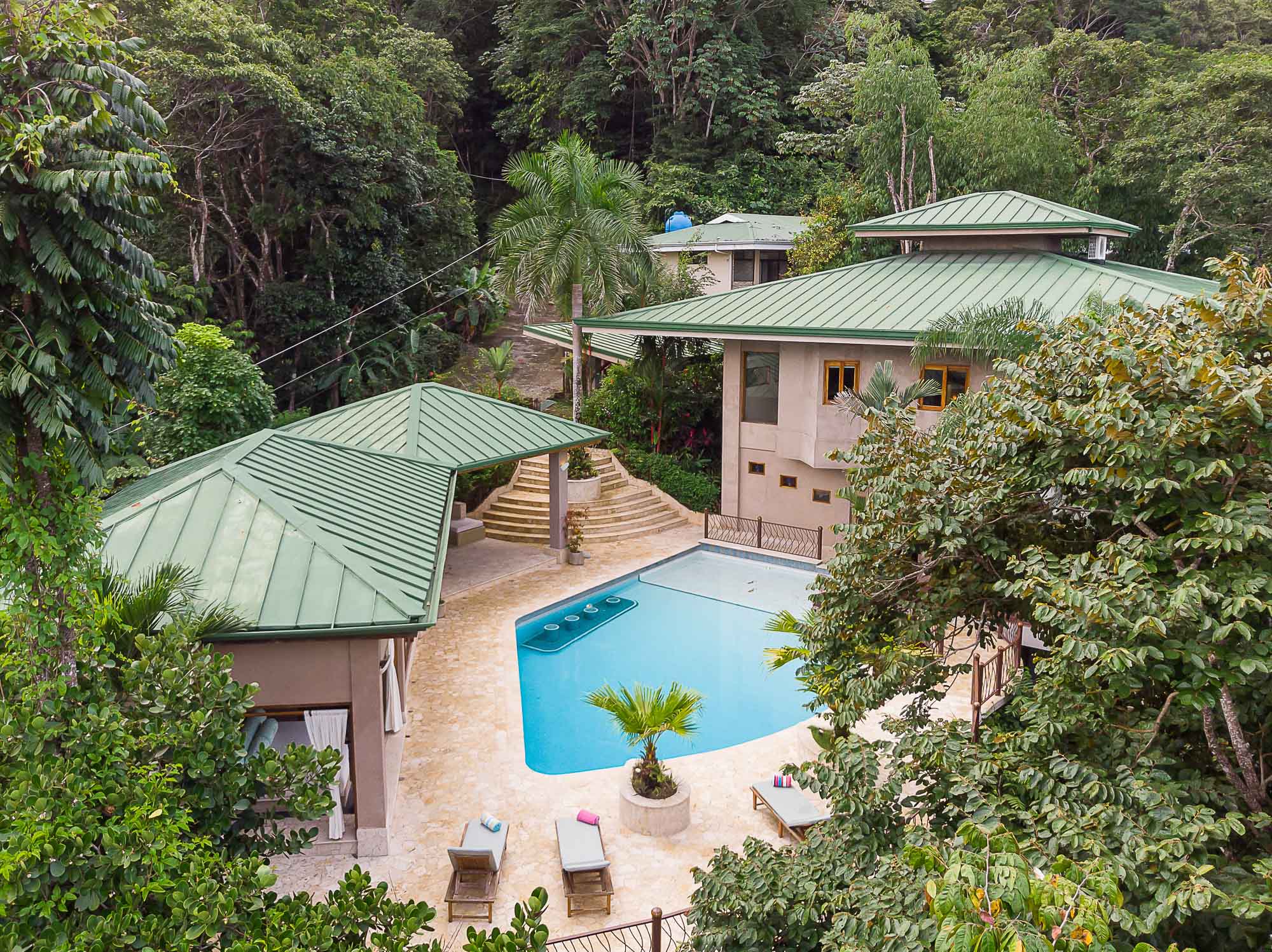 The Estrella del Mar villa complex features a large pool and patio bordered by multiple buildings with green roofs, all nestled within a lush tropical rainforest.