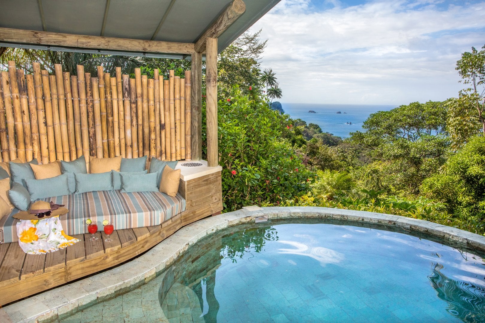 A shaded outdoor lounge with a rounded daybed and a small plunge pool overlooks the expansive ocean and lush jungle.