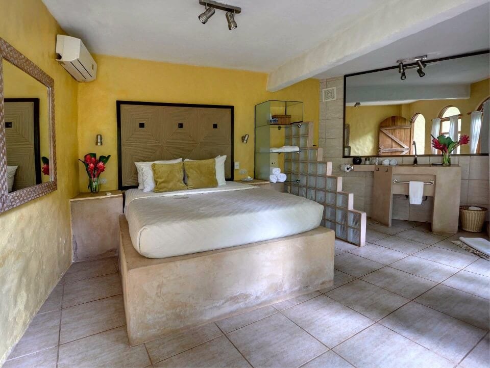 This bright bedroom suite features a built-in bed, textured yellow walls, an open vanity area, and a large mirror reflecting an arched window and natural light.