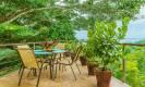 An outdoor terrace provides an open-air dining area framed by lush jungle foliage with views to the distant ocean.