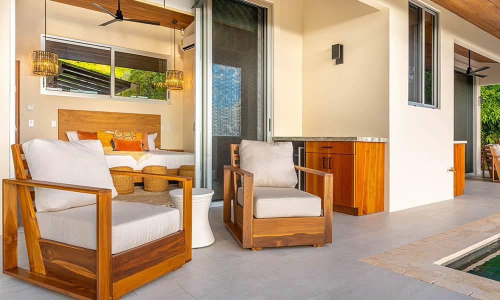 An open-air terrace with comfortable seating and an outdoor bar connects to a king bedroom with tropical views, all steps from a refreshing pool.