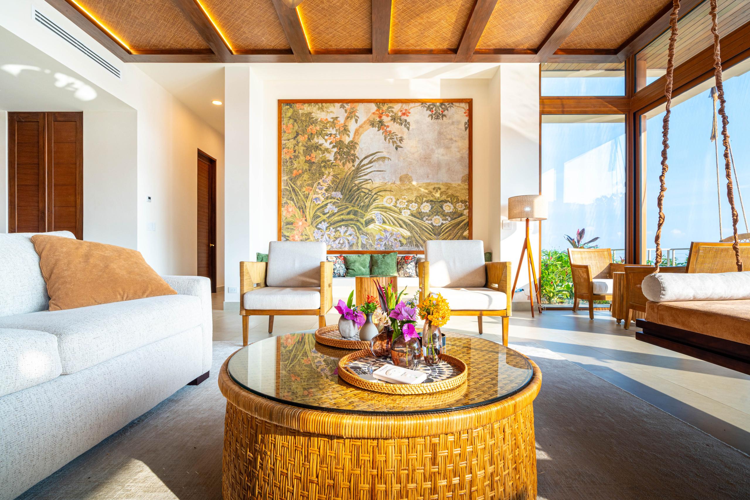 This living room features a woven ceiling with wood beams, ample natural light from expansive windows, and views of the tropical landscape.