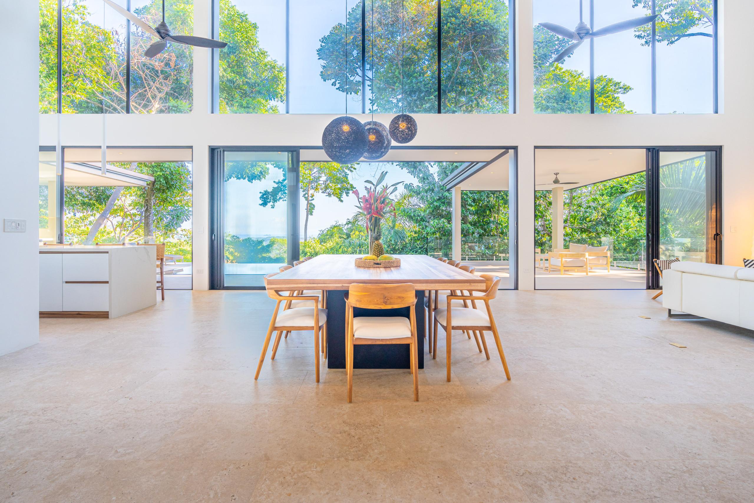 The expansive dining and living area offers abundant natural light and panoramic views of the tropical jungle and distant ocean through floor-to-ceiling glass doors.