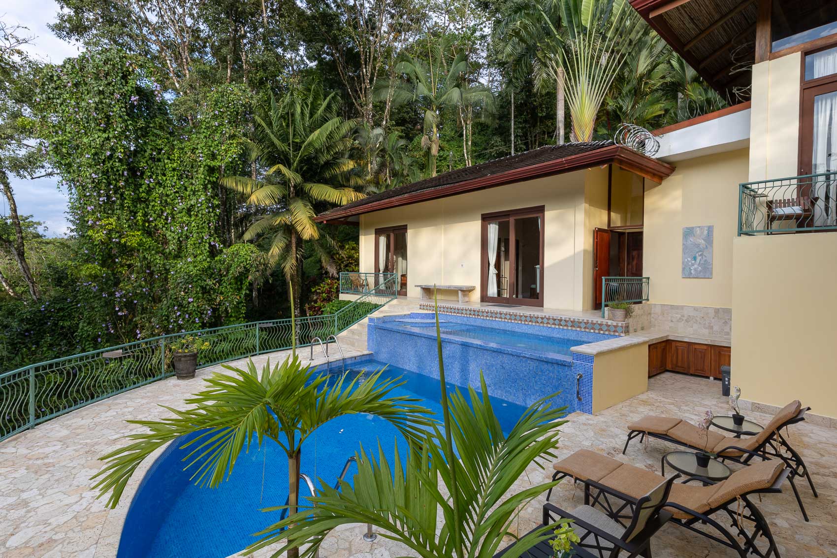 A multi-level pool and stone patio offer direct access to villa rooms, framed by lush tropical foliage and abundant natural light.