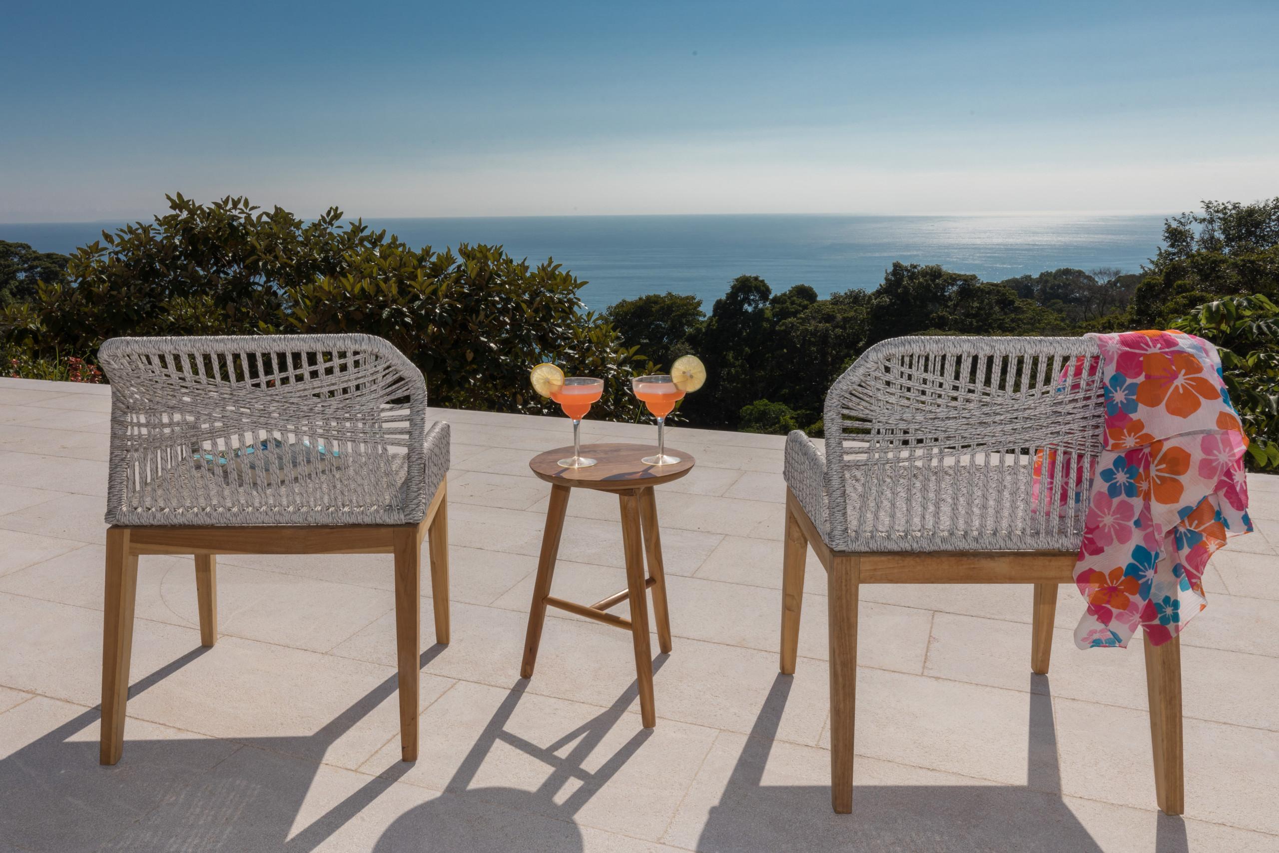 A sun-drenched outdoor terrace with light-toned tiled flooring provides seating and expansive views of the Pacific Ocean and vibrant jungle.