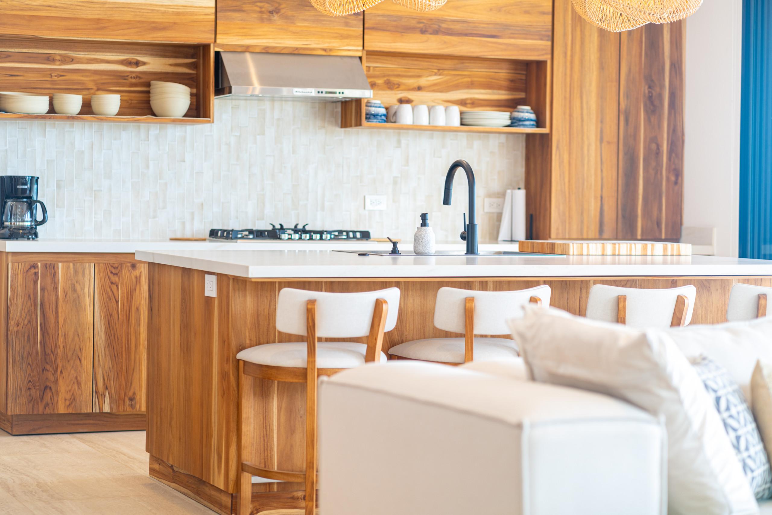 The well-lit kitchen features warm natural wood cabinetry, a white subway tile backsplash, and a central island with bar stools, creating an inviting and functional area.