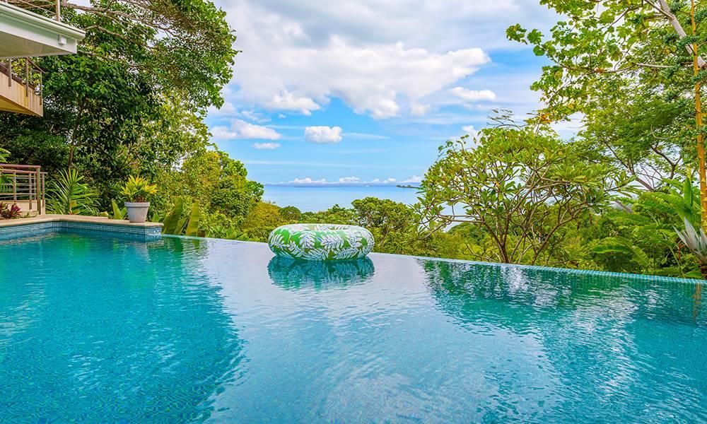 The infinity pool's blue tiles reflect natural light, offering expansive views of the Pacific Ocean and surrounding jungle.