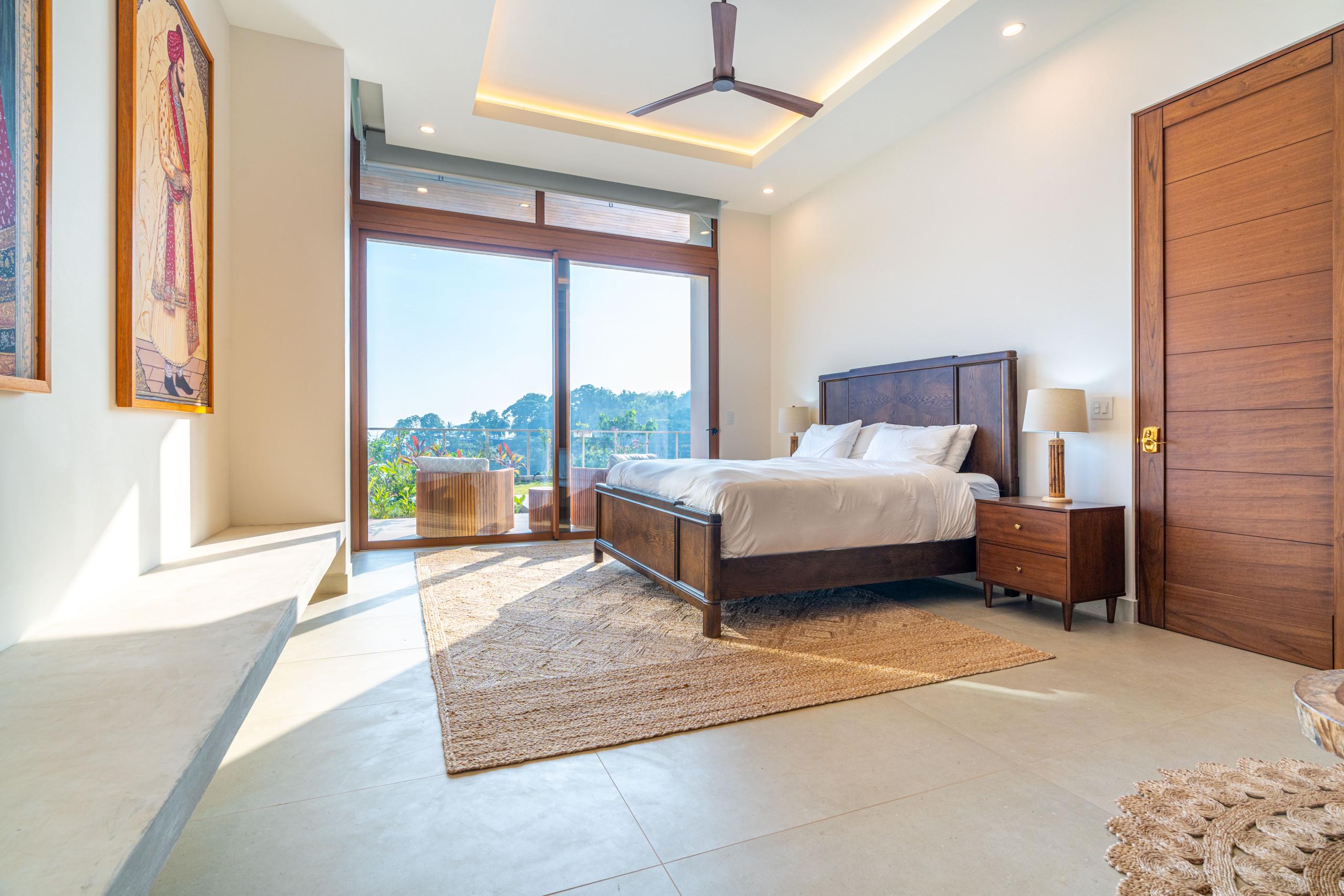 This bedroom features a king bed, rich wood furnishings, and floor-to-ceiling glass doors that welcome abundant natural light and offer a jungle view.