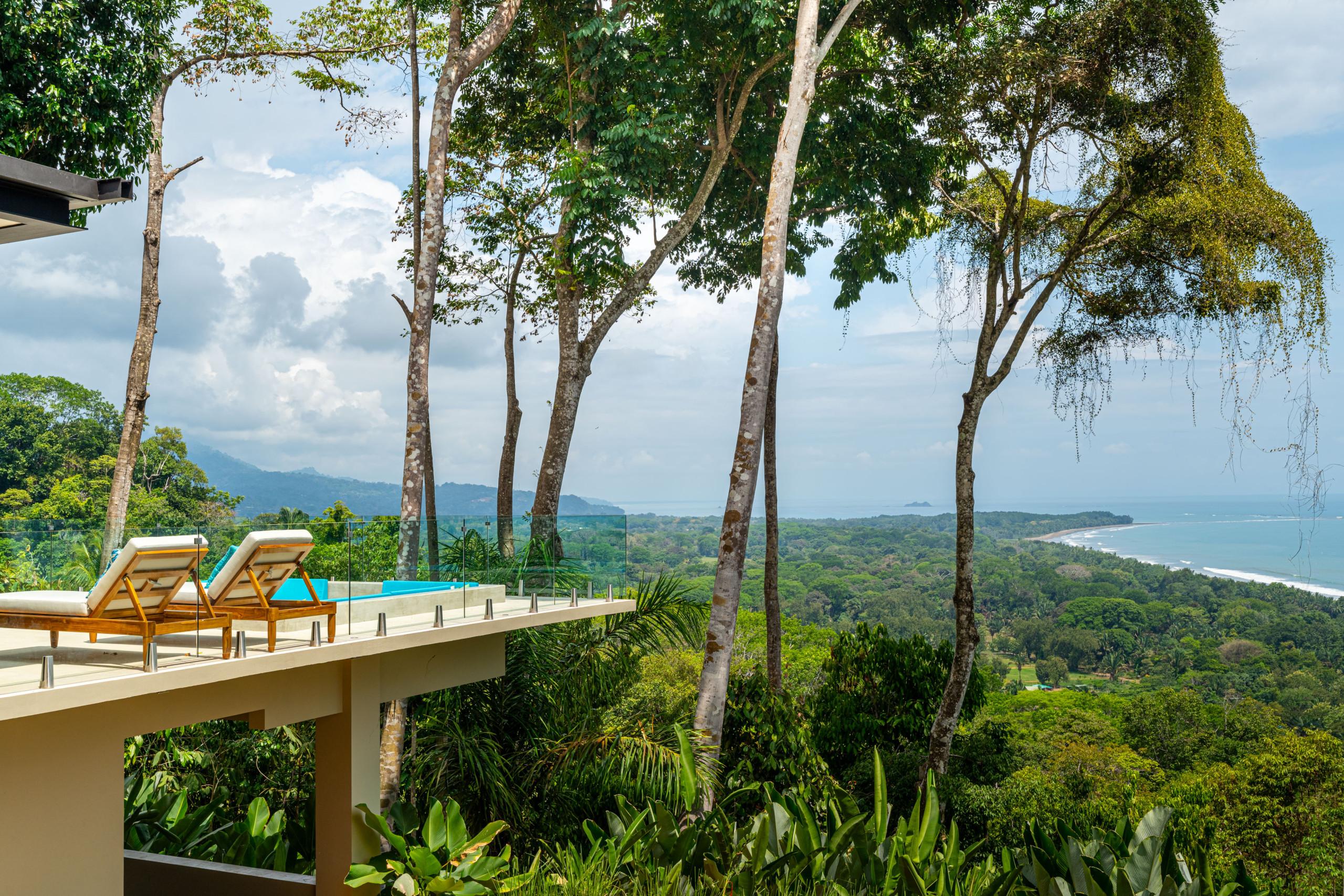 The infinity pool and lounging terrace overlook an expansive view of the coastline, tropical forest, and ocean.